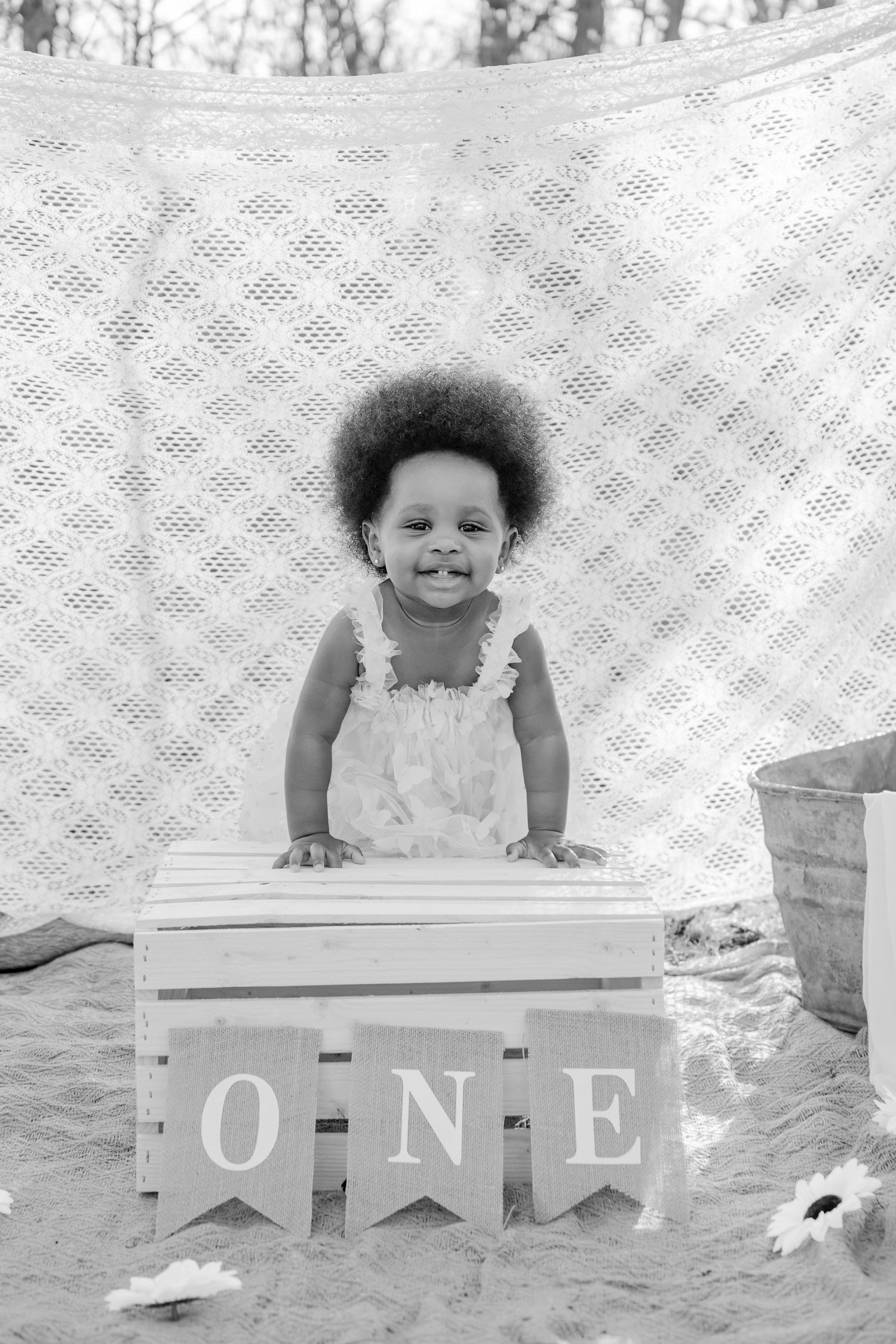 Sweet baby girl smiling in black and white photo beside wooden crate with ONE banner for first birthday photoshoot.