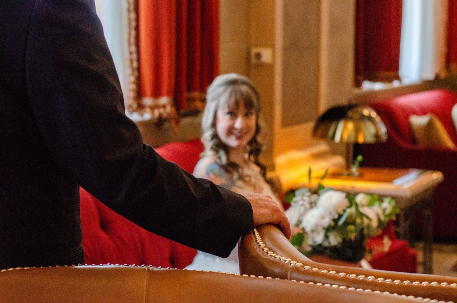 Groom holding hands with smiling flower girl seated in ornate red chair during wedding reception.