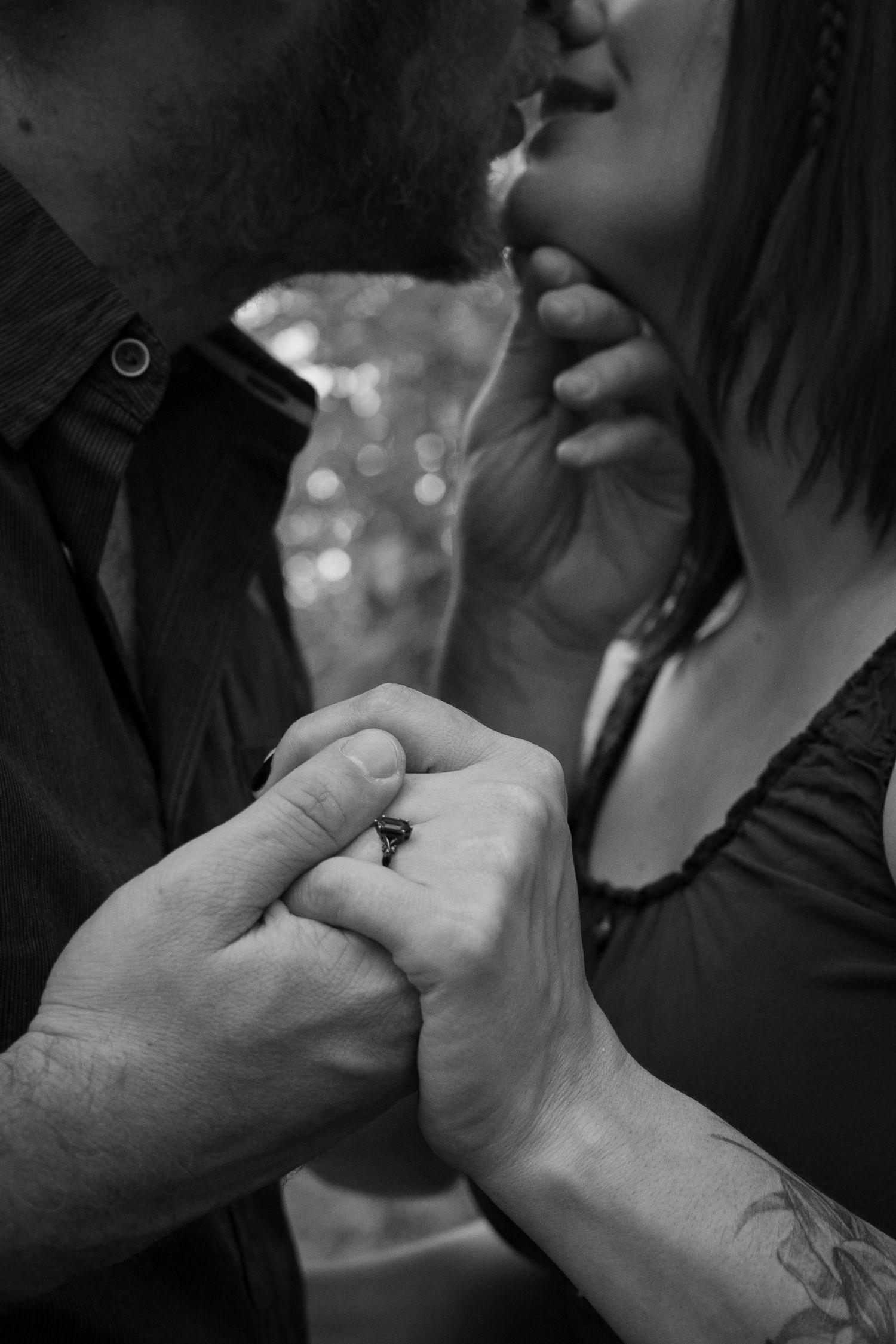 Black and white photo of a couple almost kissing while holding hands, showcasing a ring and tattoo.