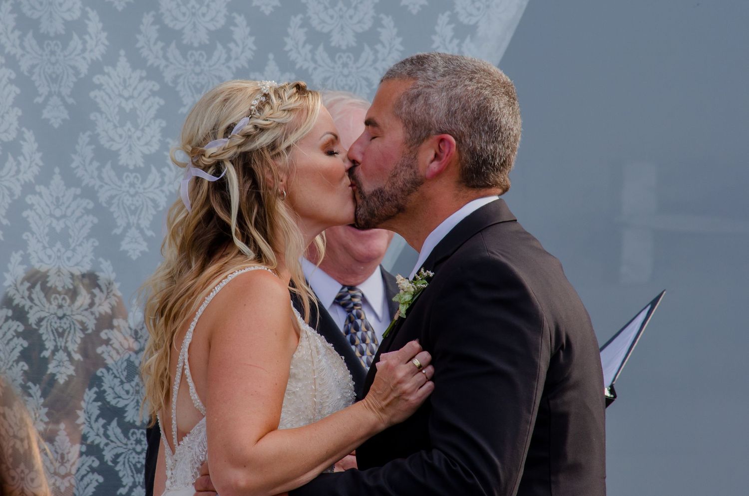 Bride and groom share their first kiss at outdoor wedding ceremony, bride wearing floral hair accessory.