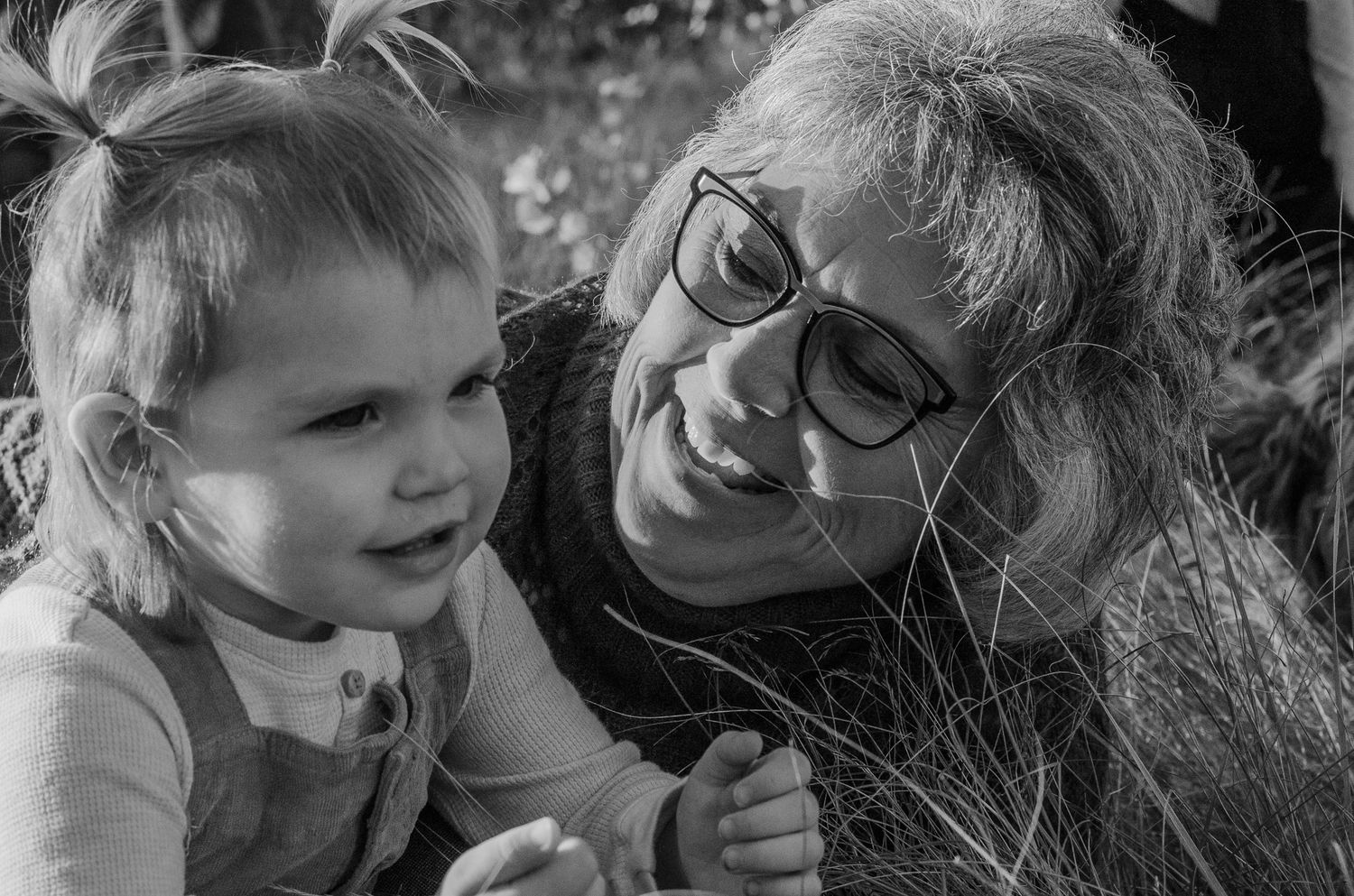 Black and white photo of a grandmother smiling warmly at a toddler girl outdoors.
