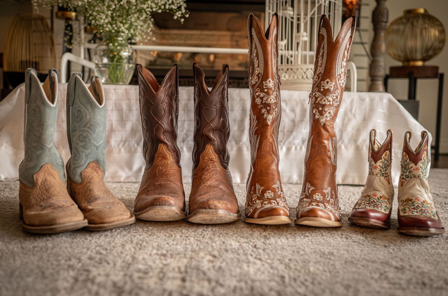 Four pairs of colorful cowboy boots lined up on a rustic floor, featuring floral embroidery and Western designs.