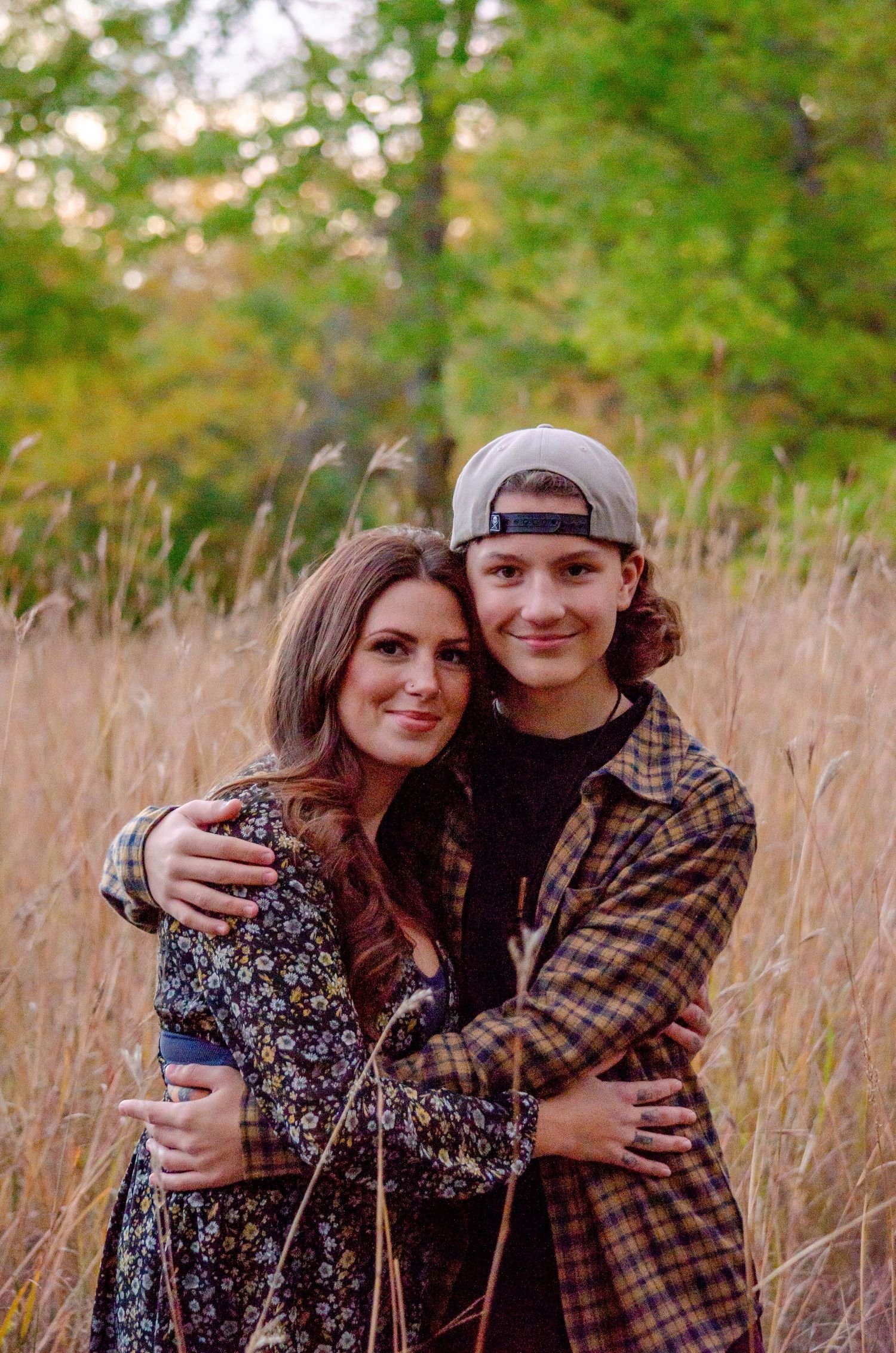 A young couple embracing and smiling in a golden field with autumn trees in the background.