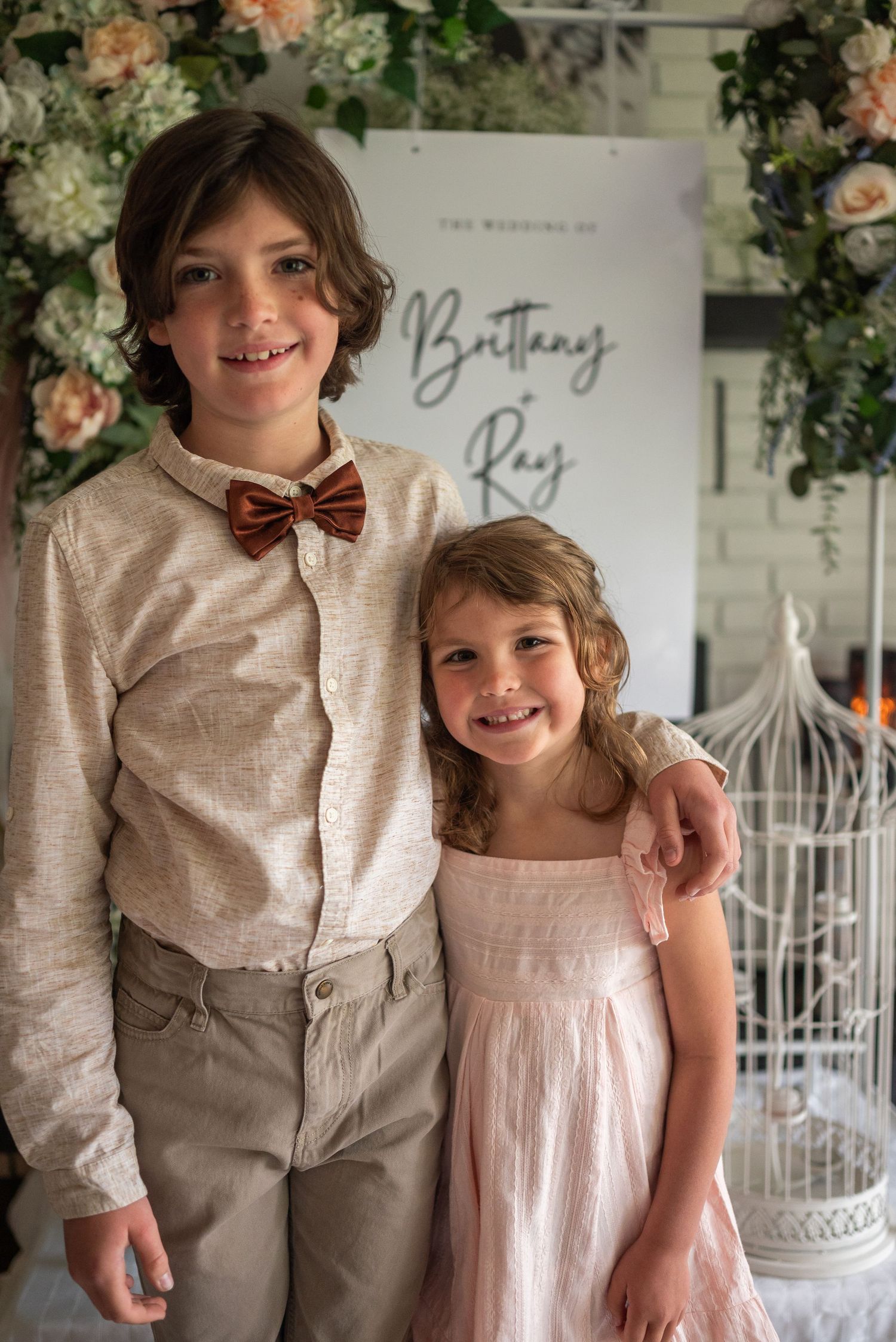 A boy in a bow tie and a girl in a pink dress pose together at the wedding of Brittany and Ray.