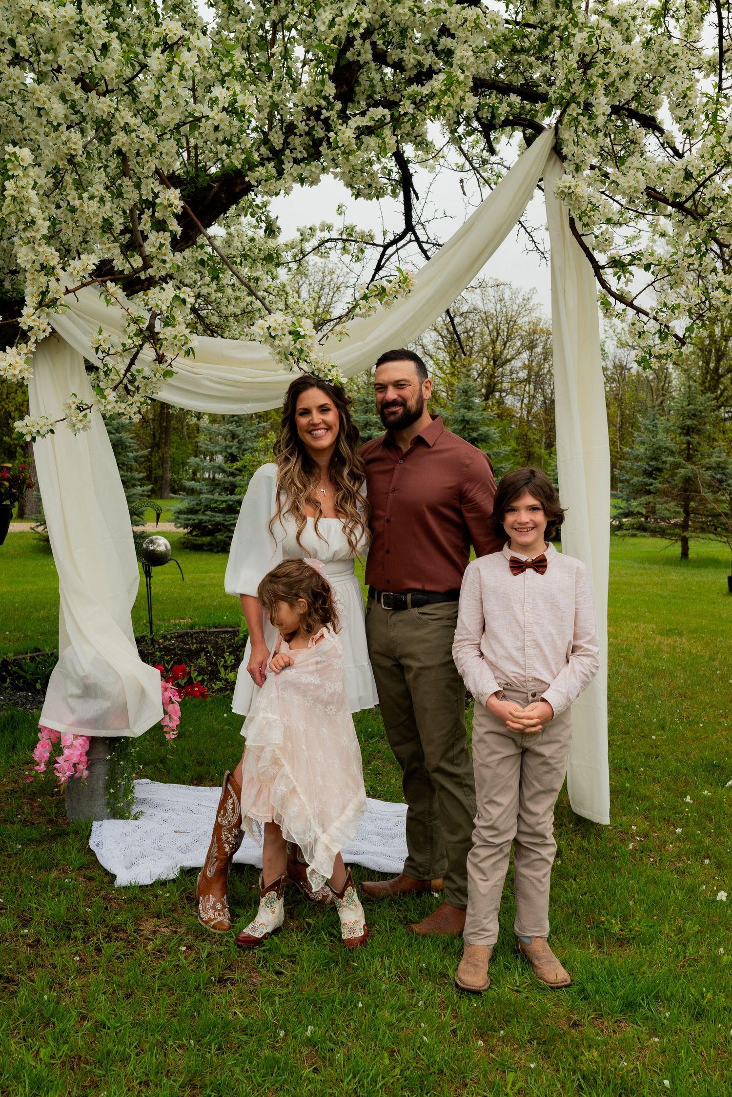 Family posing under a white draped floral arch outdoors during a spring wedding ceremony.