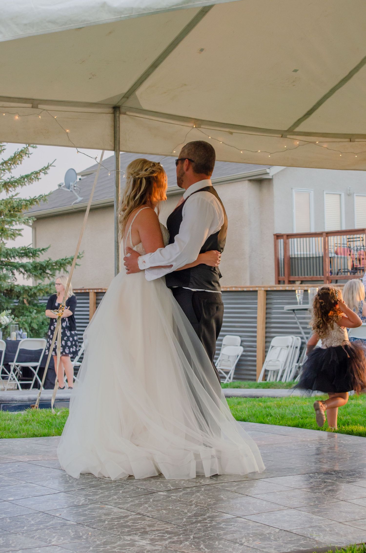 Bride and groom share their first dance under a white tent at an outdoor backyard wedding reception.