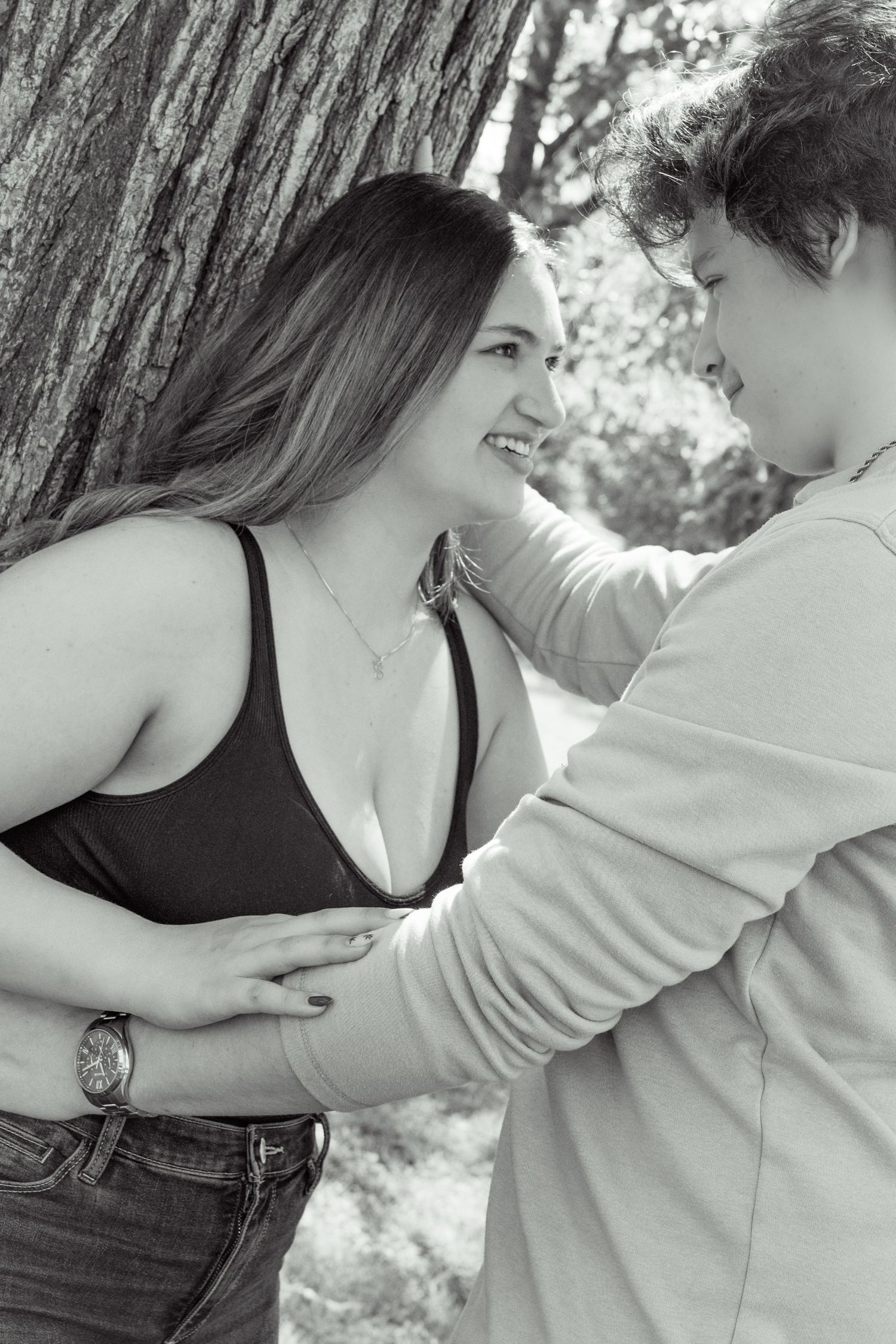 Black and white photo of a smiling couple sharing a tender moment outdoors near a large tree.