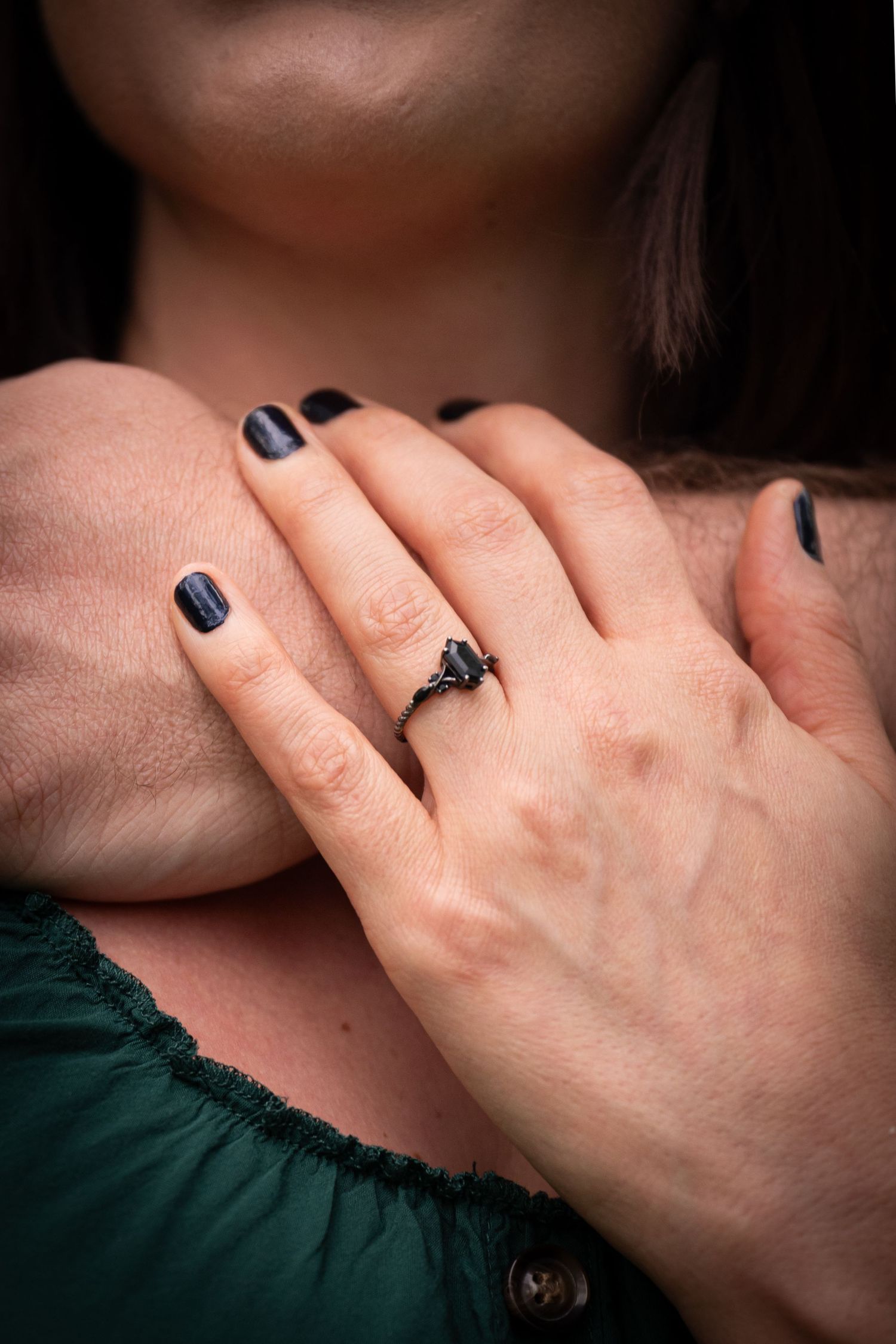 Woman wearing a black gothic ring with dark nail polish, hands crossed over chest in green top.