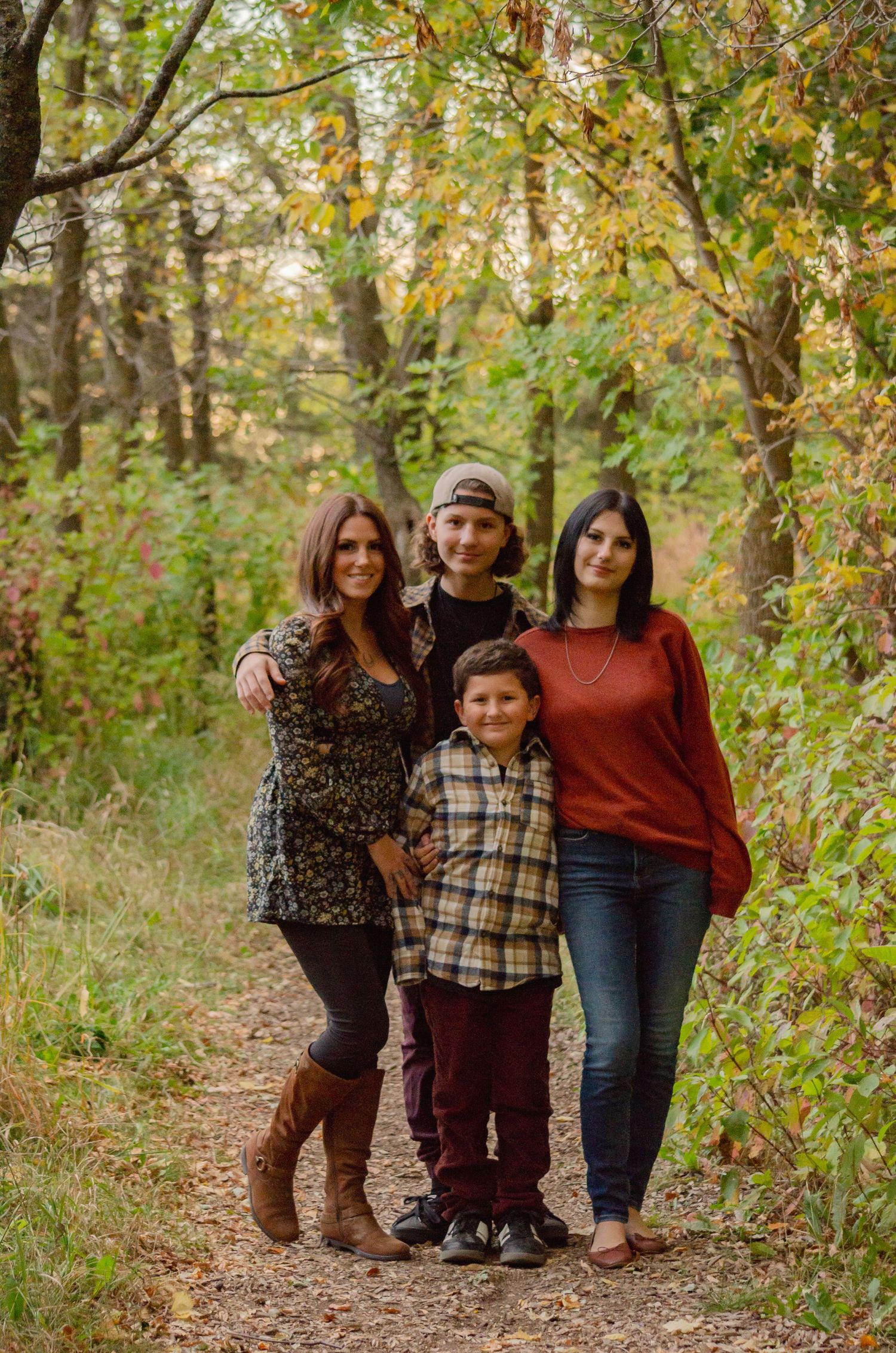 Family of four posing on a forest trail surrounded by autumn foliage, wearing casual fall outfits.