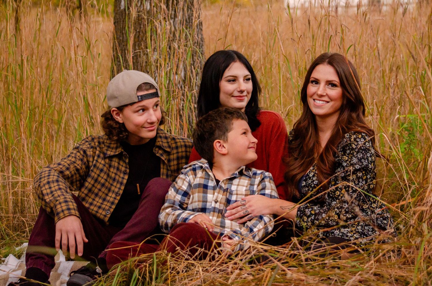 Family of four smiling and sitting together in a golden grass field during autumn.