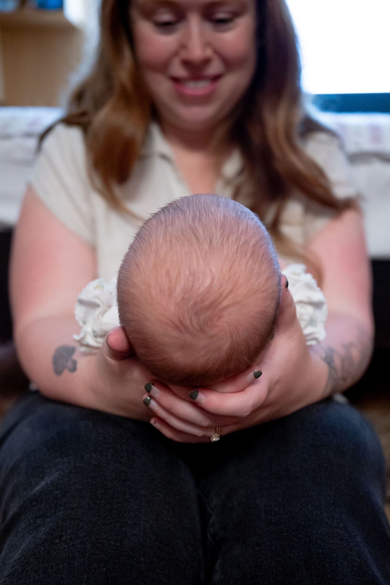 A smiling mother gently holds her newborn baby, cradling the infant's head in her tattooed hands.