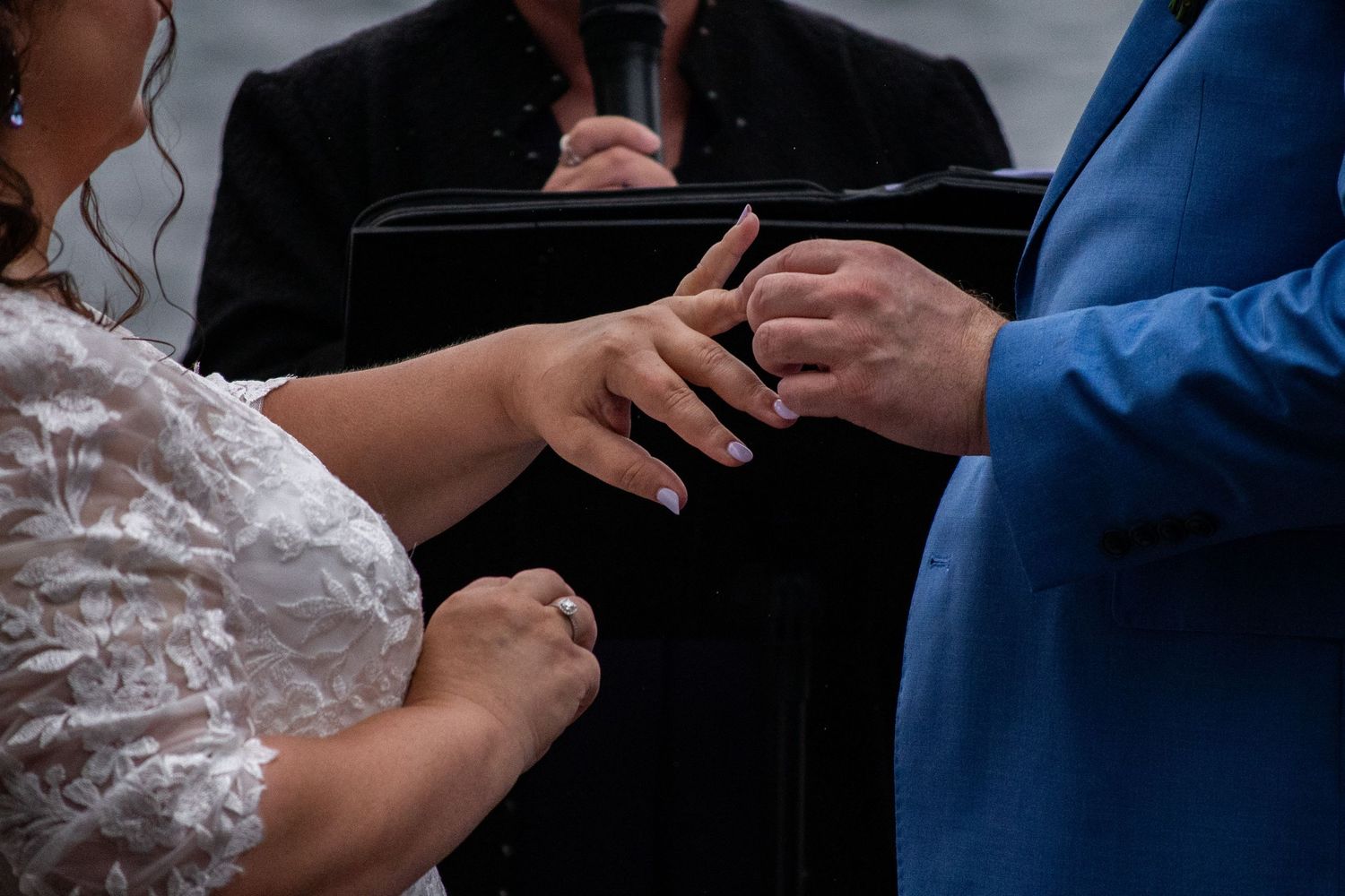 Bride and groom exchanging wedding rings during ceremony with officiant in background.