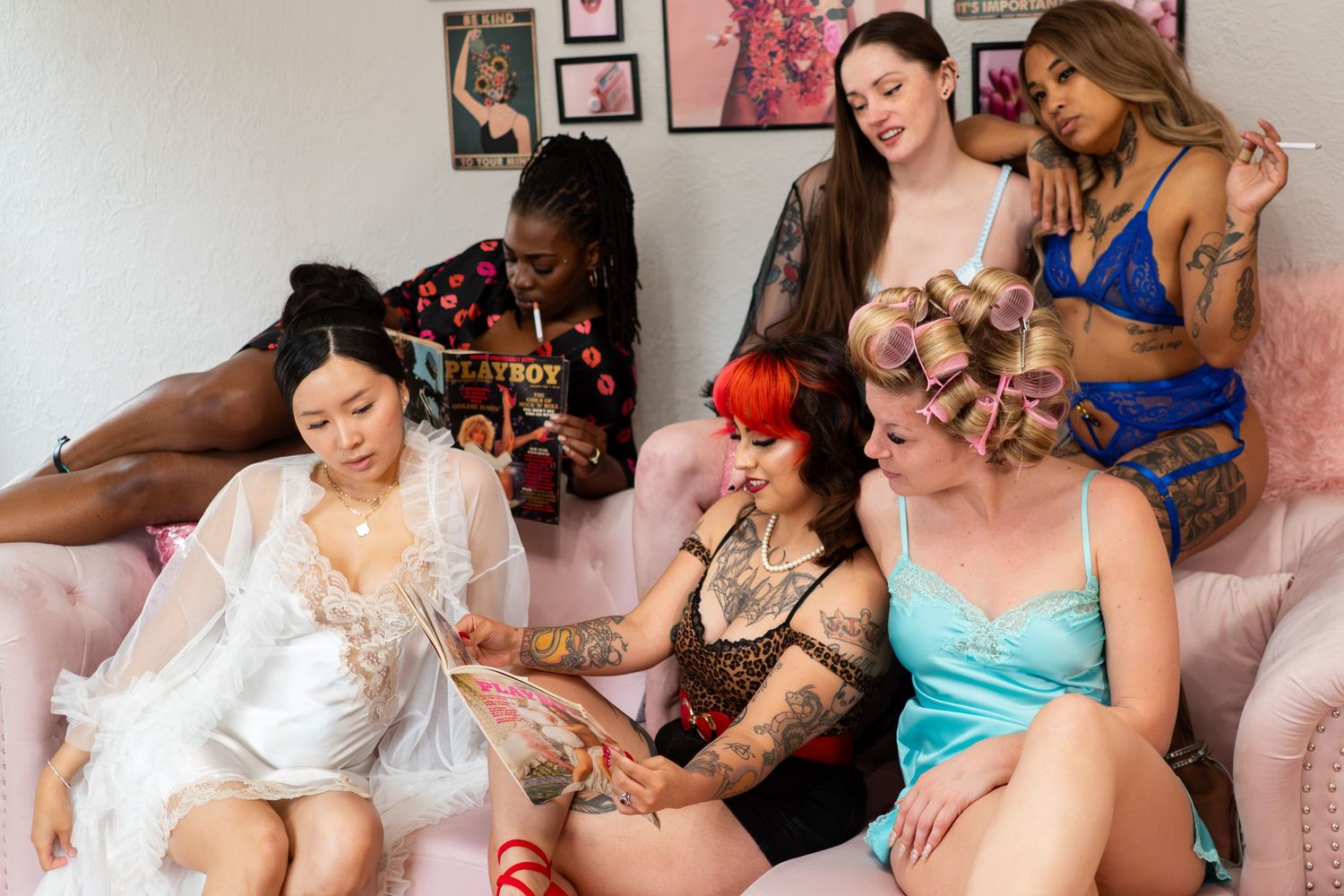 Diverse group of women in lingerie socializing on a pink sofa in a decorated room.