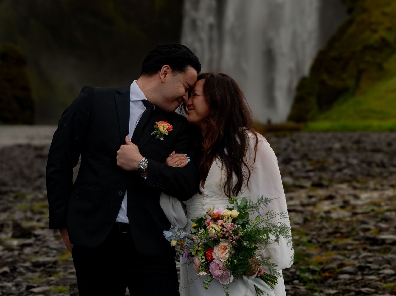 Couple in wedding attire sharing a romantic moment in front of a waterfall in Iceland.