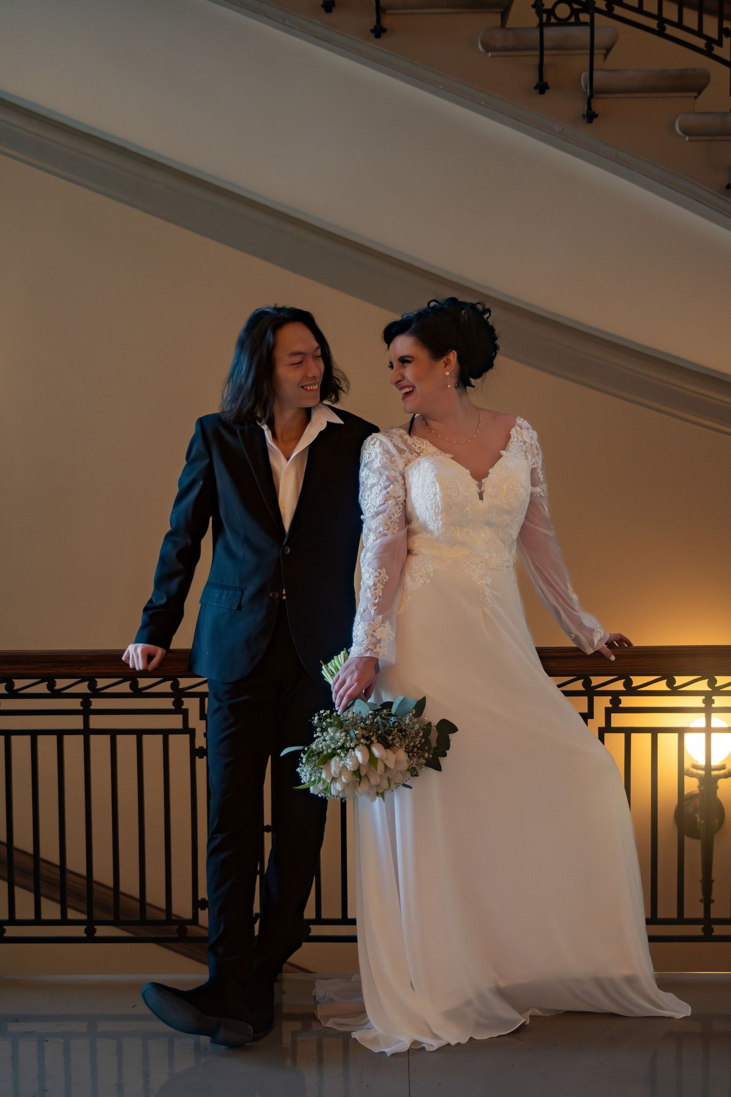 Bride and groom standing together on ornate balcony railing in elegant wedding venue.