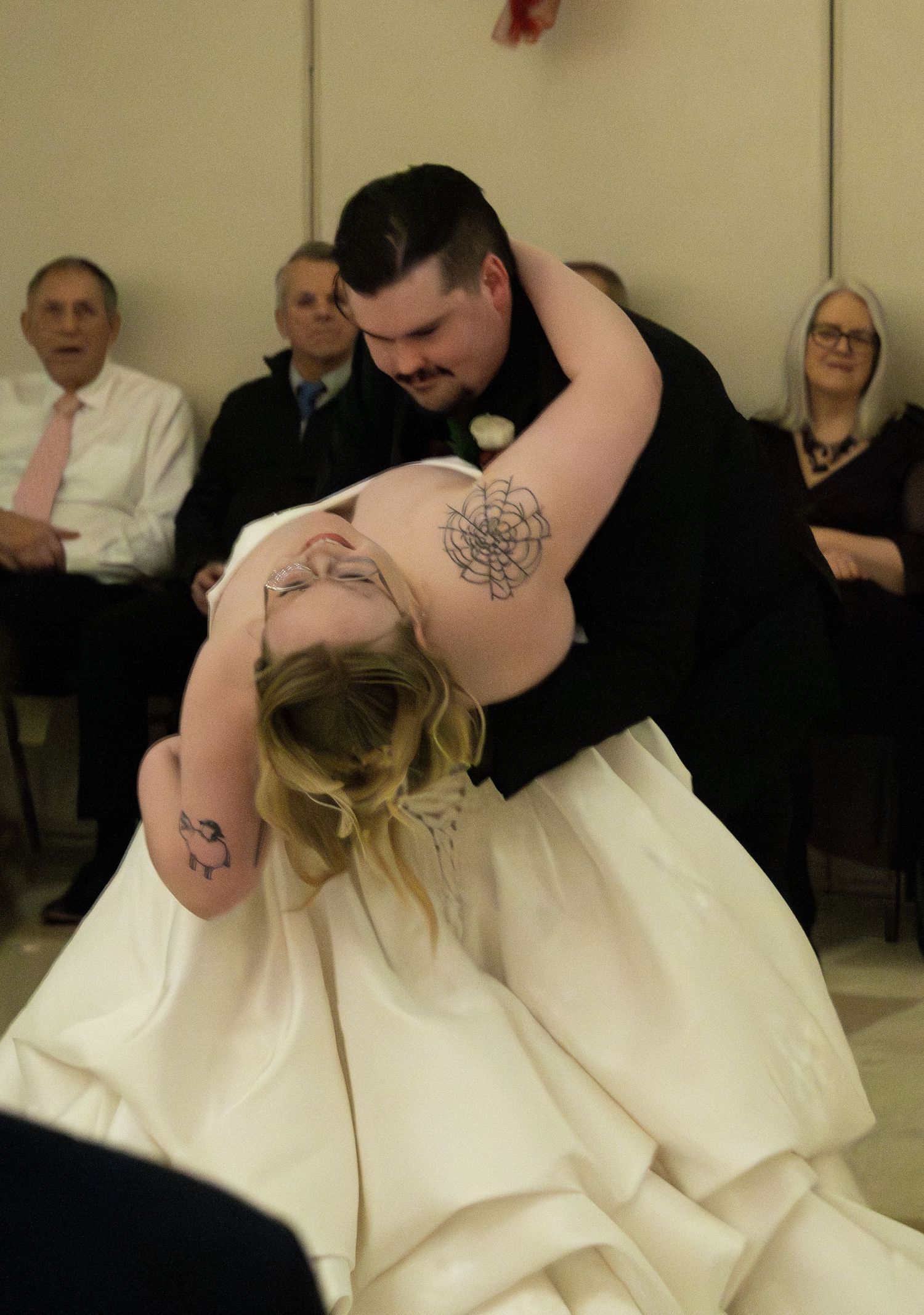 Groom dipping bride during first dance at wedding reception while guests watch in the background.