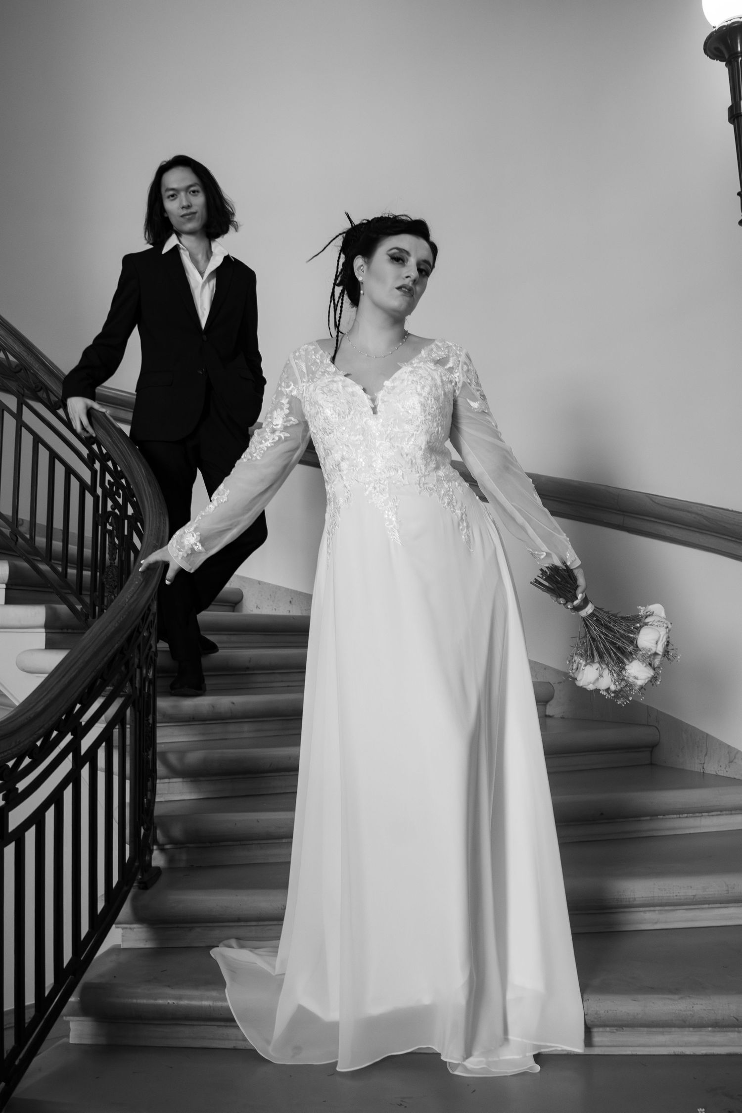 Black and white photo of bride descending elegant staircase with groom behind her.