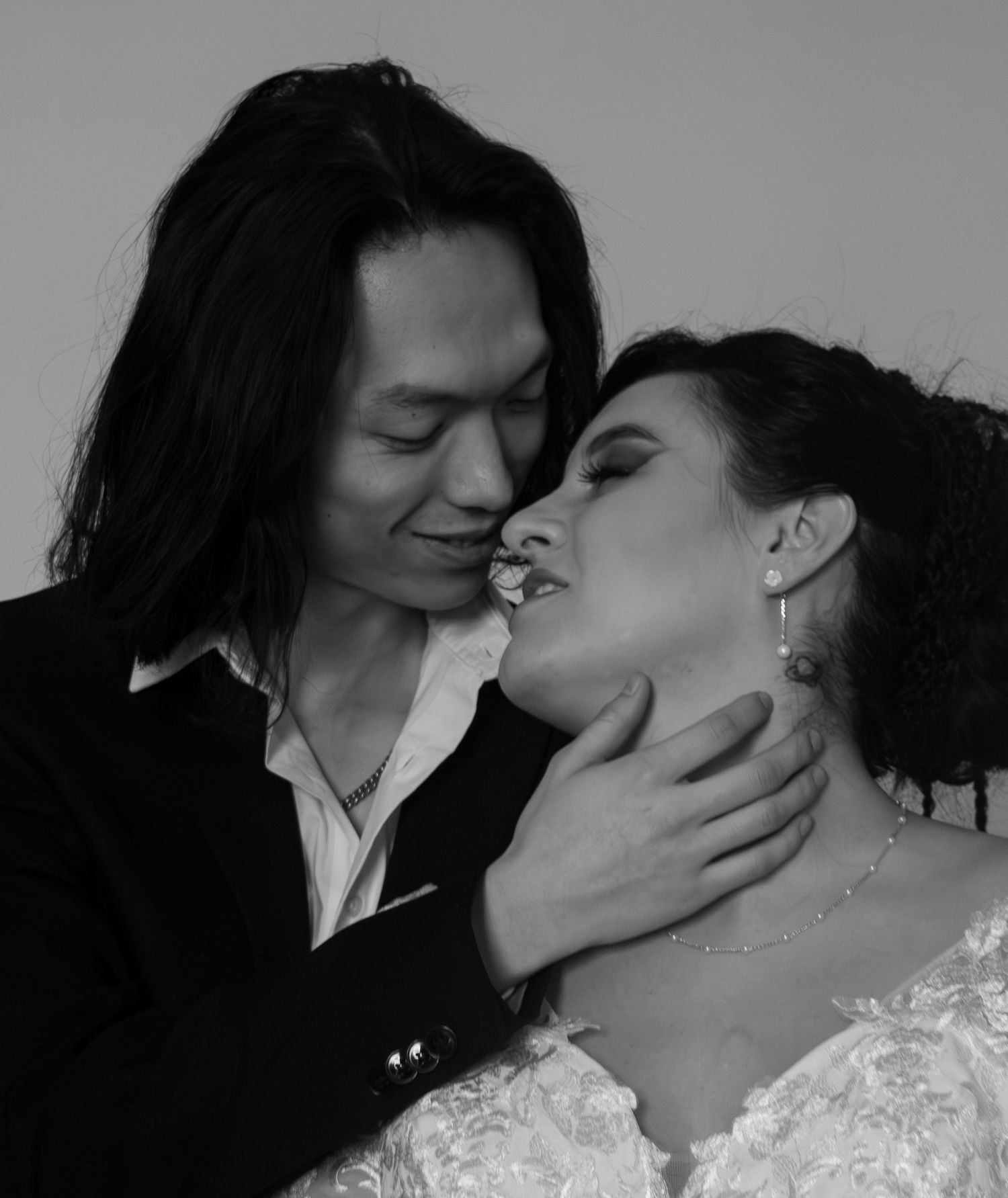 Black and white romantic photo of a couple in wedding attire, man tenderly holding woman's face close for a kiss.