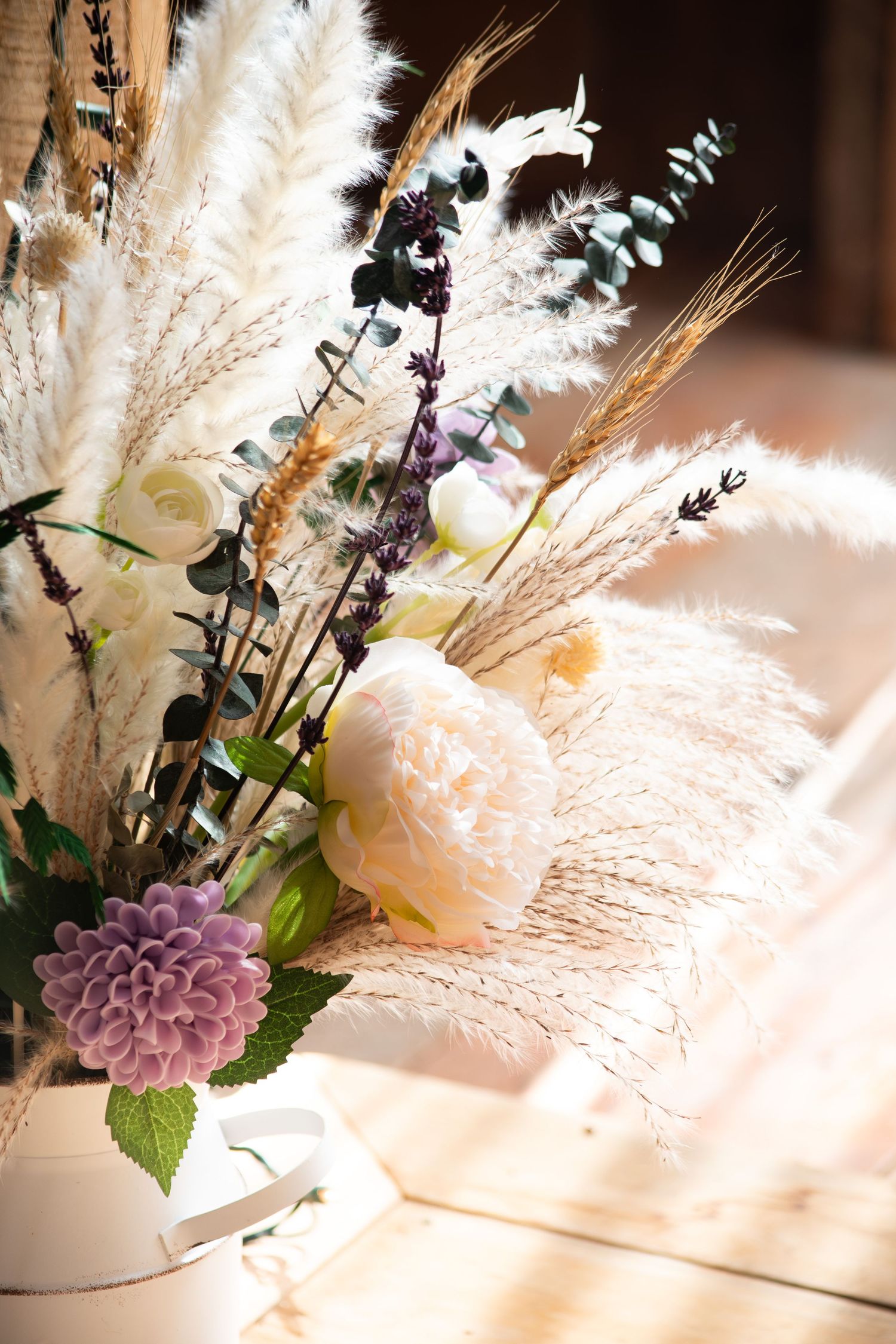 Rustic boho wedding floral arrangement with pampas grass, white peonies, purple dahlias, and dried wheat in warm sunlight.