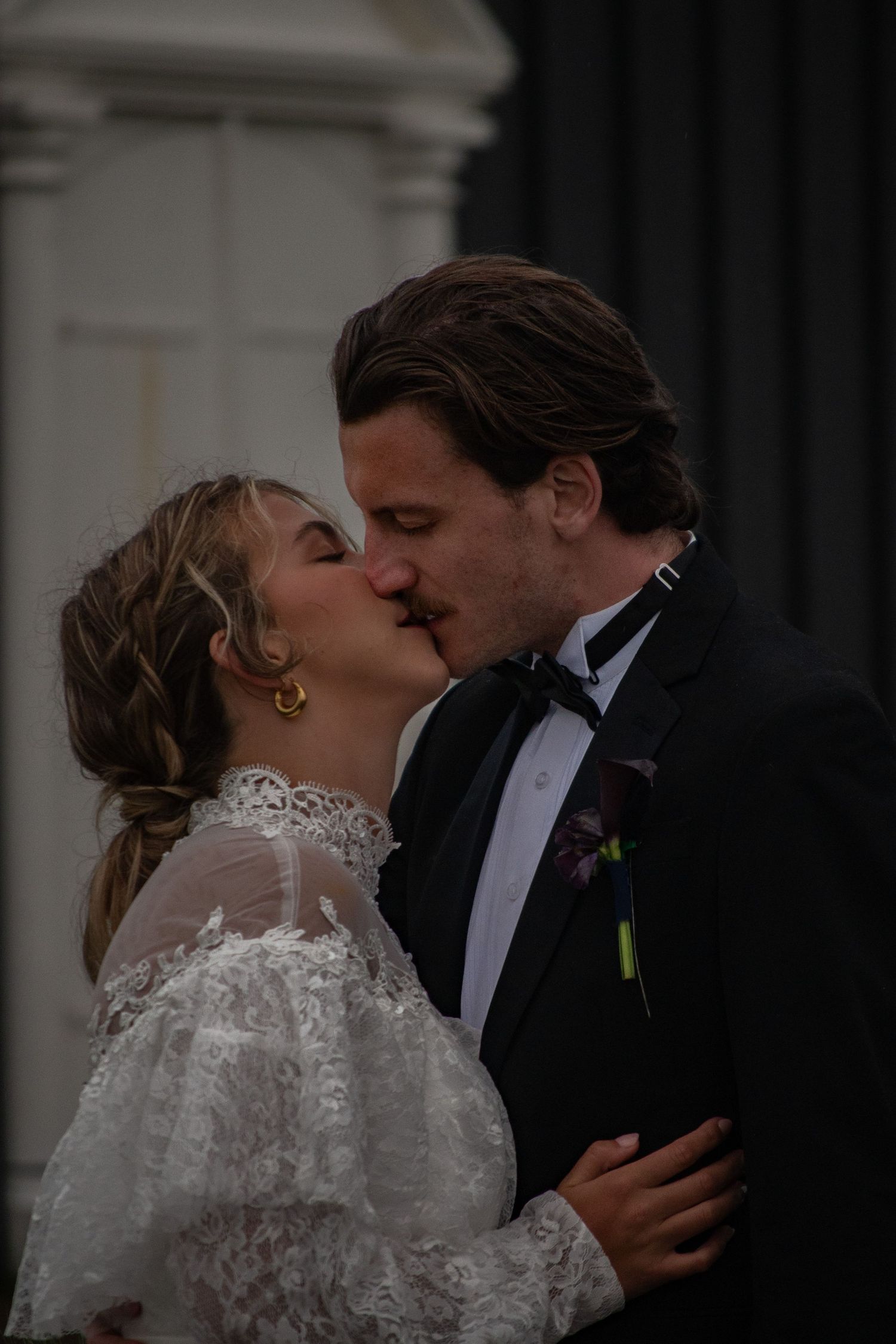 Bride and groom sharing a romantic first kiss in wedding attire, lace bridal gown and black tuxedo.