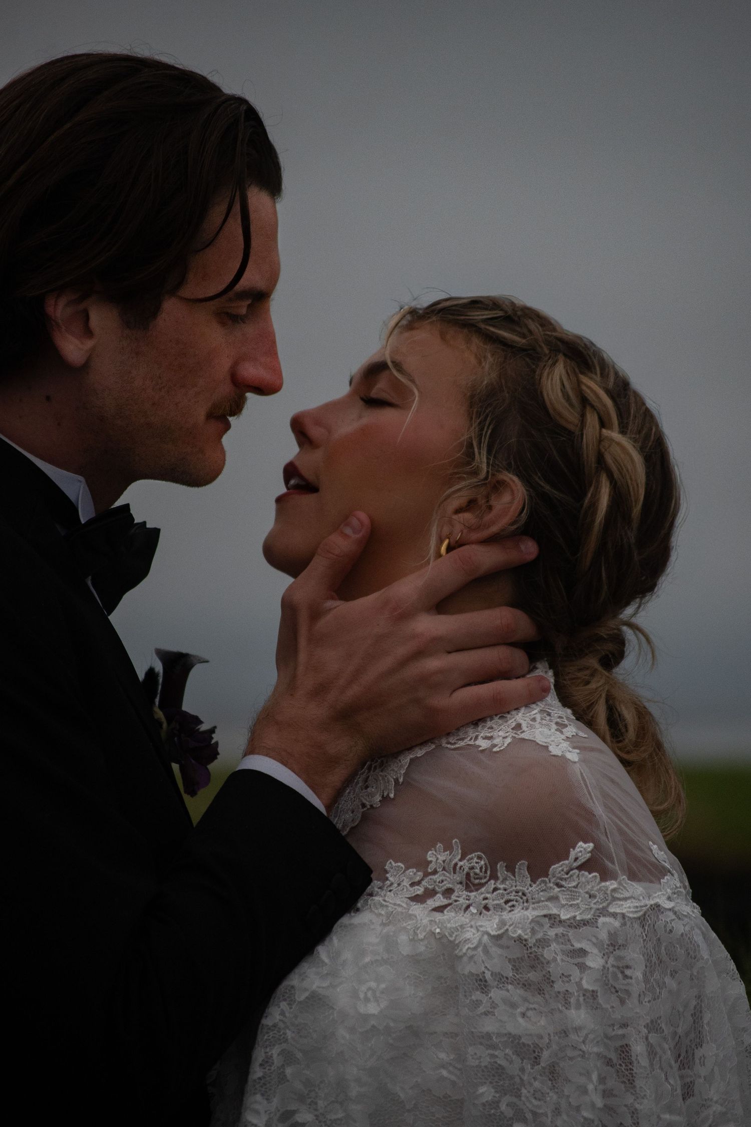 Bride and groom share a romantic moment, groom tenderly holding brides face in lace wedding dress outdoors.