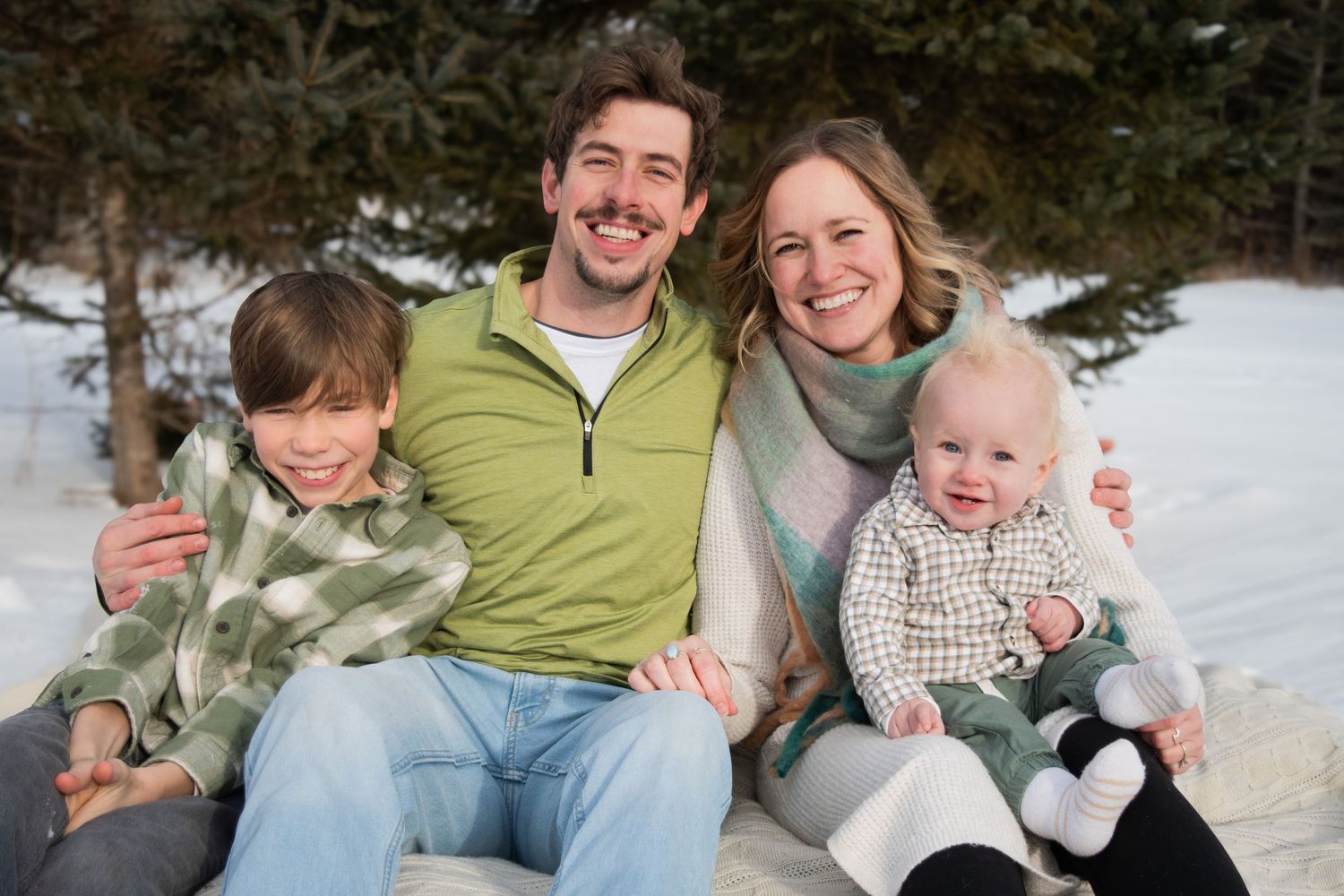 Family of four smiling outdoors in winter snow, parents with two children in cozy colorful outfits.