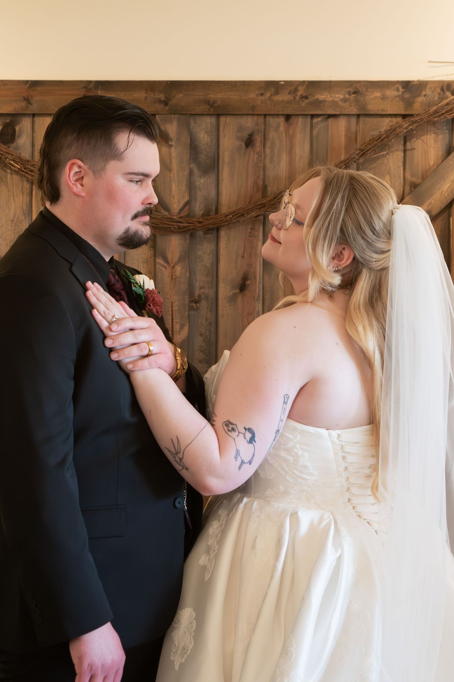 Bride and groom share an intimate moment near a rustic wooden wall on their wedding day.