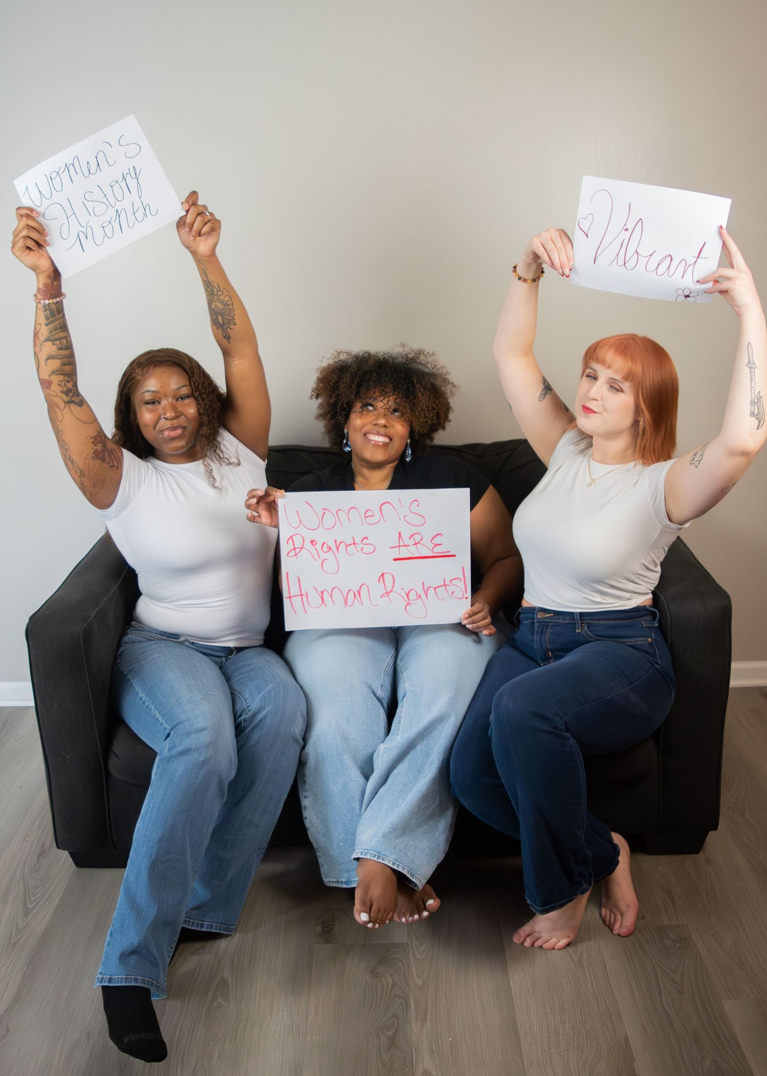 Three women on sofa holding signs reading womens rights are human rights and pro-choice.