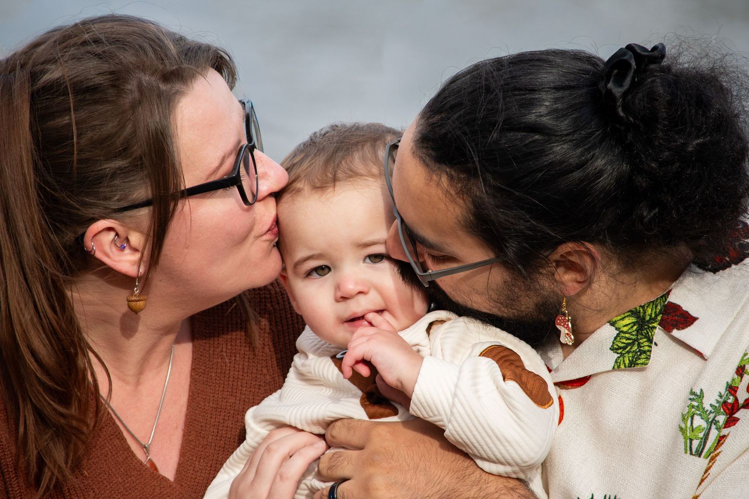 Two parents kissing their smiling baby on the cheeks in a heartwarming family portrait photo.