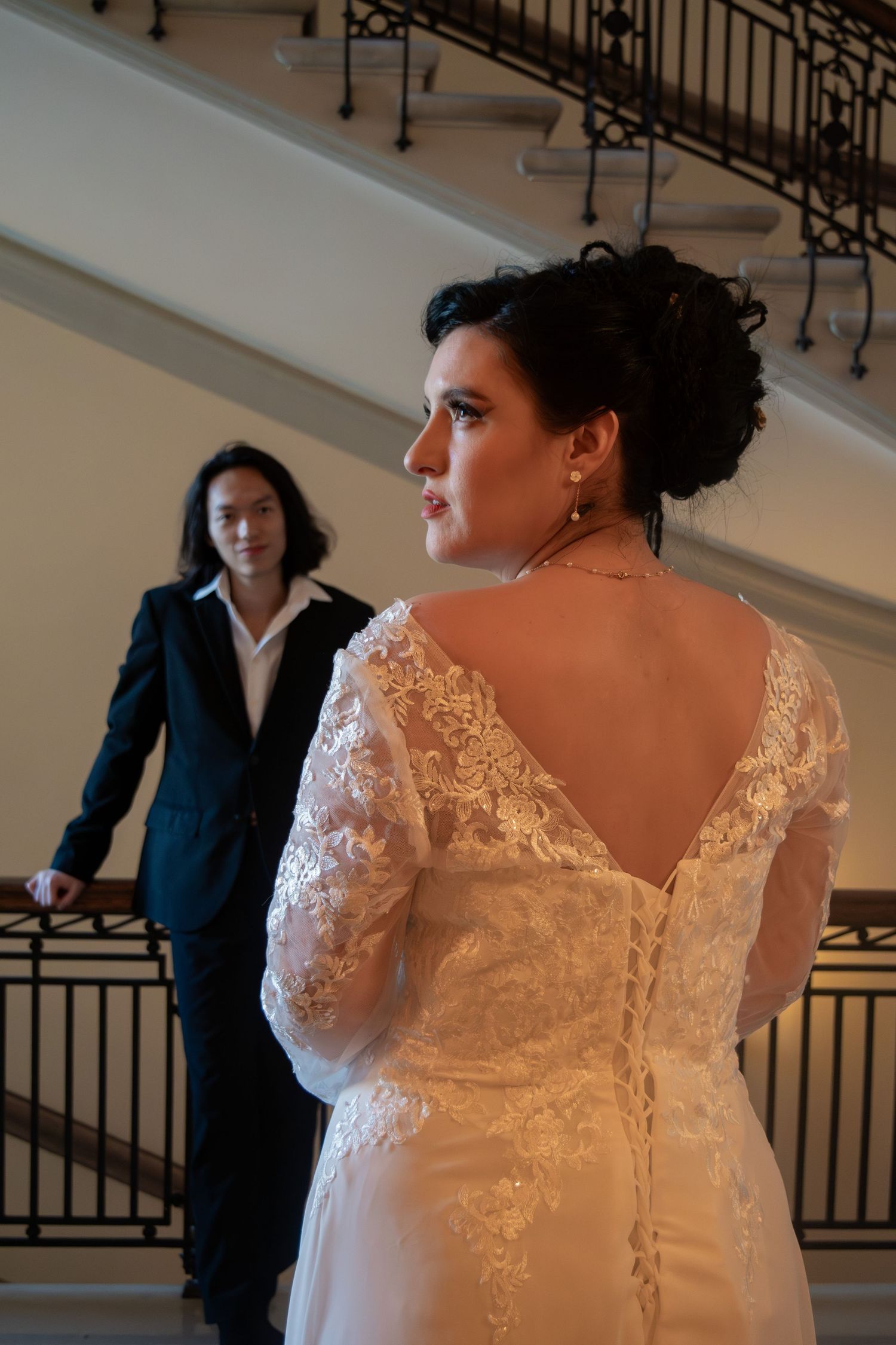 Bride in lace back wedding gown with groom standing on grand staircase behind her.
