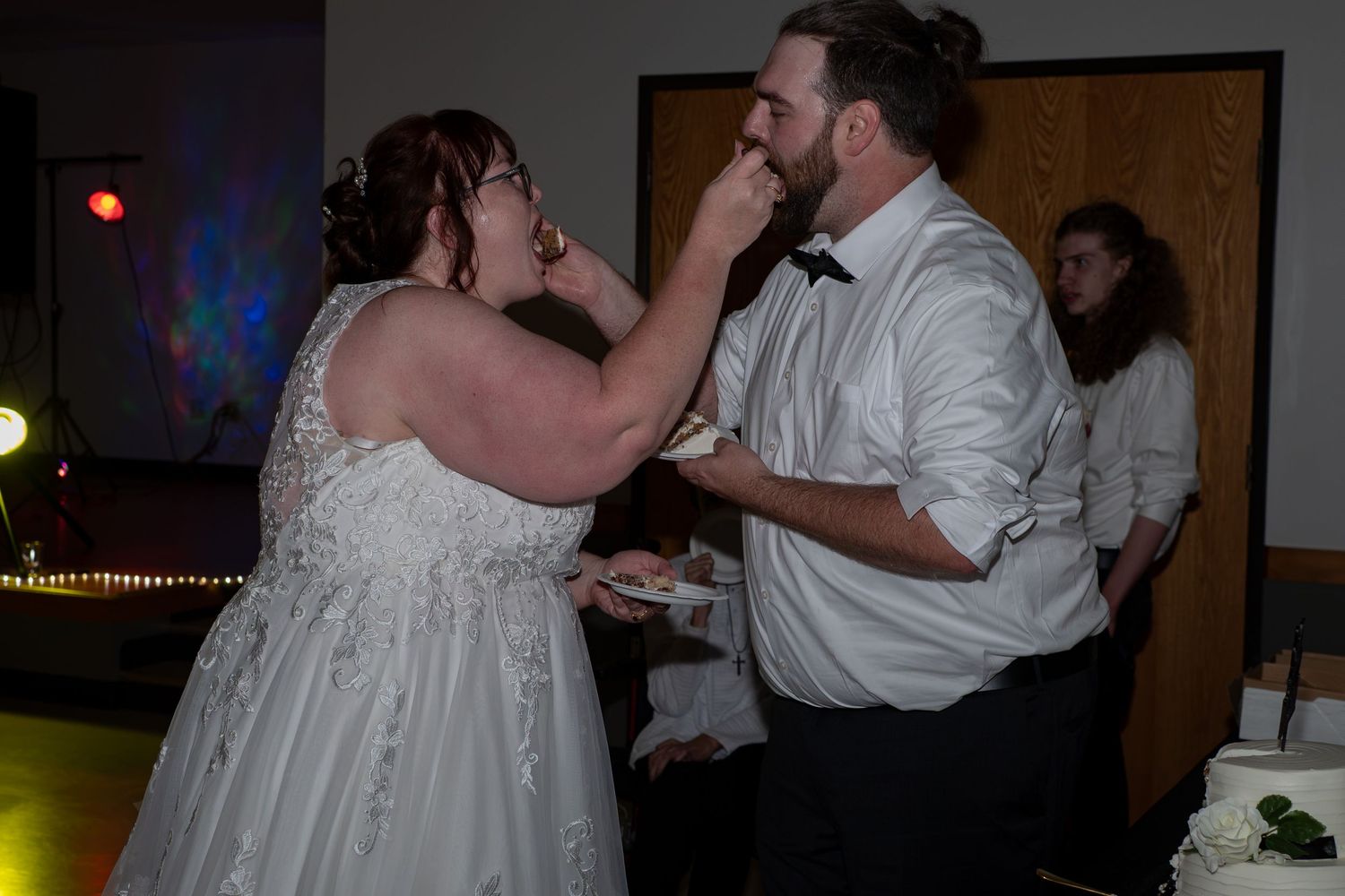 Bride feeds wedding cake to groom during reception celebration on dance floor.