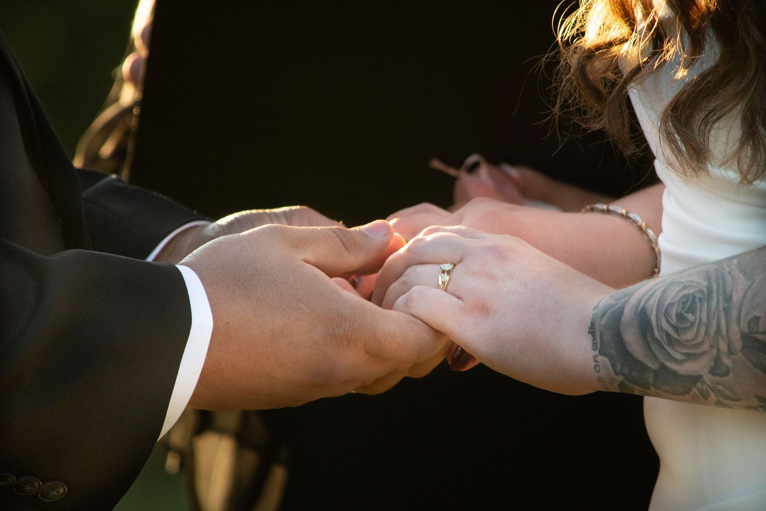 Close-up of groom placing wedding ring on brides finger during outdoor wedding ceremony.