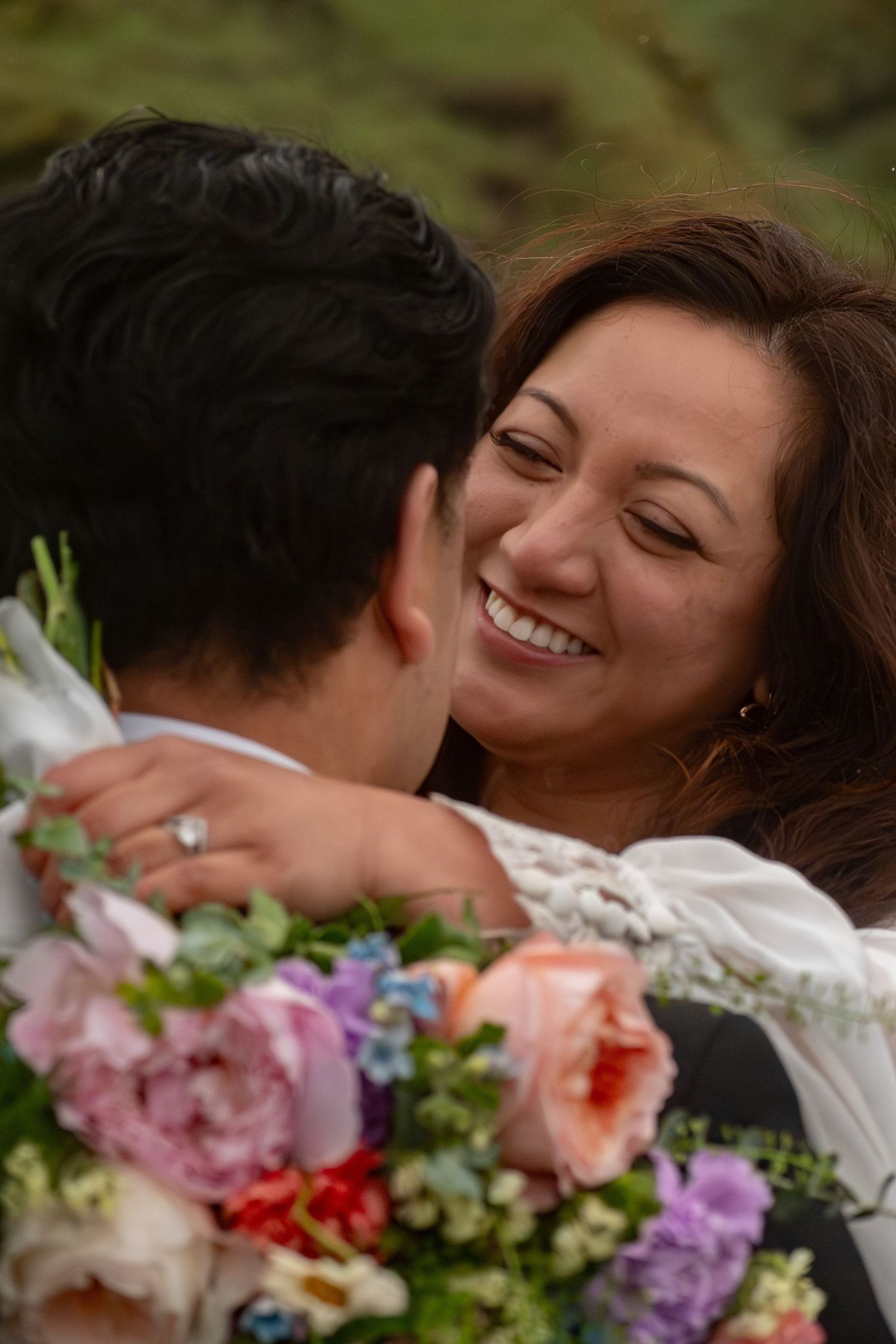 Smiling bride with floral bouquet embracing groom outdoors on wedding day.