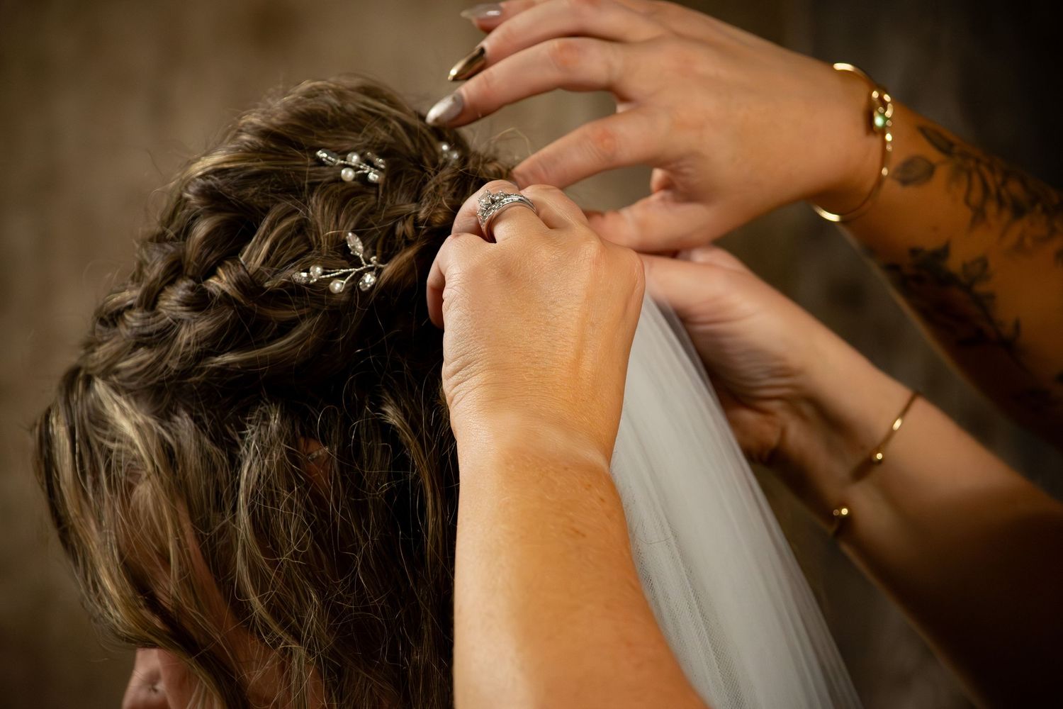 Close-up of hands placing floral hair pins into bride's elegant updo hairstyle with veil attachment.