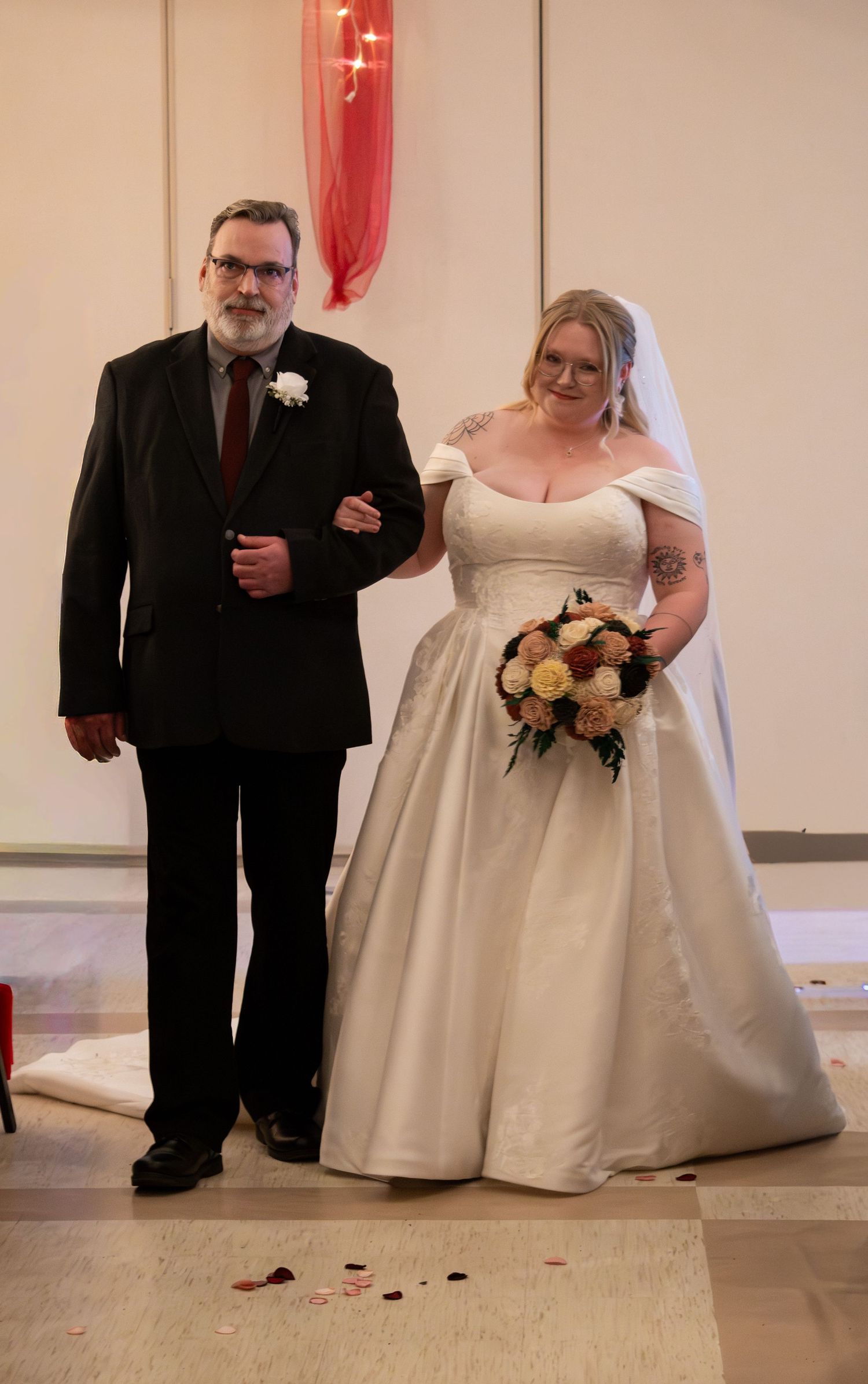 Bride in white ball gown with bouquet walks down aisle escorted by father in black suit.
