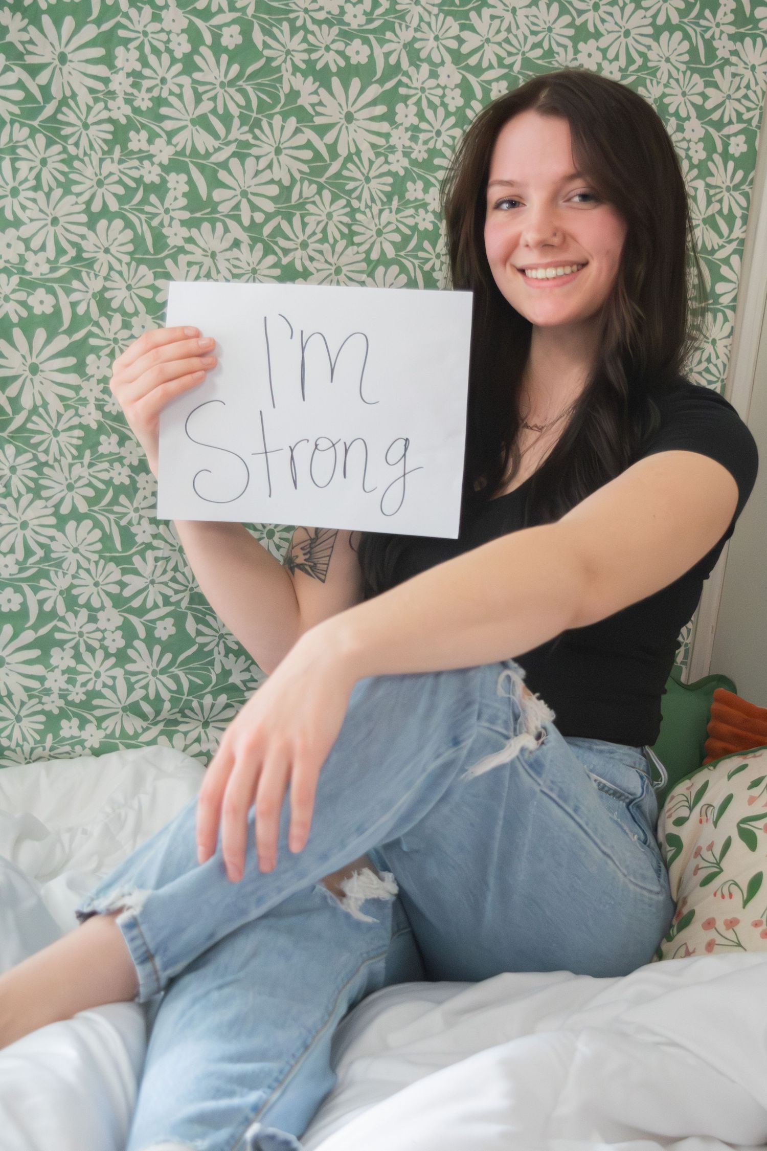 Young woman holding a sign reading I'm Strong while sitting on a bed.
