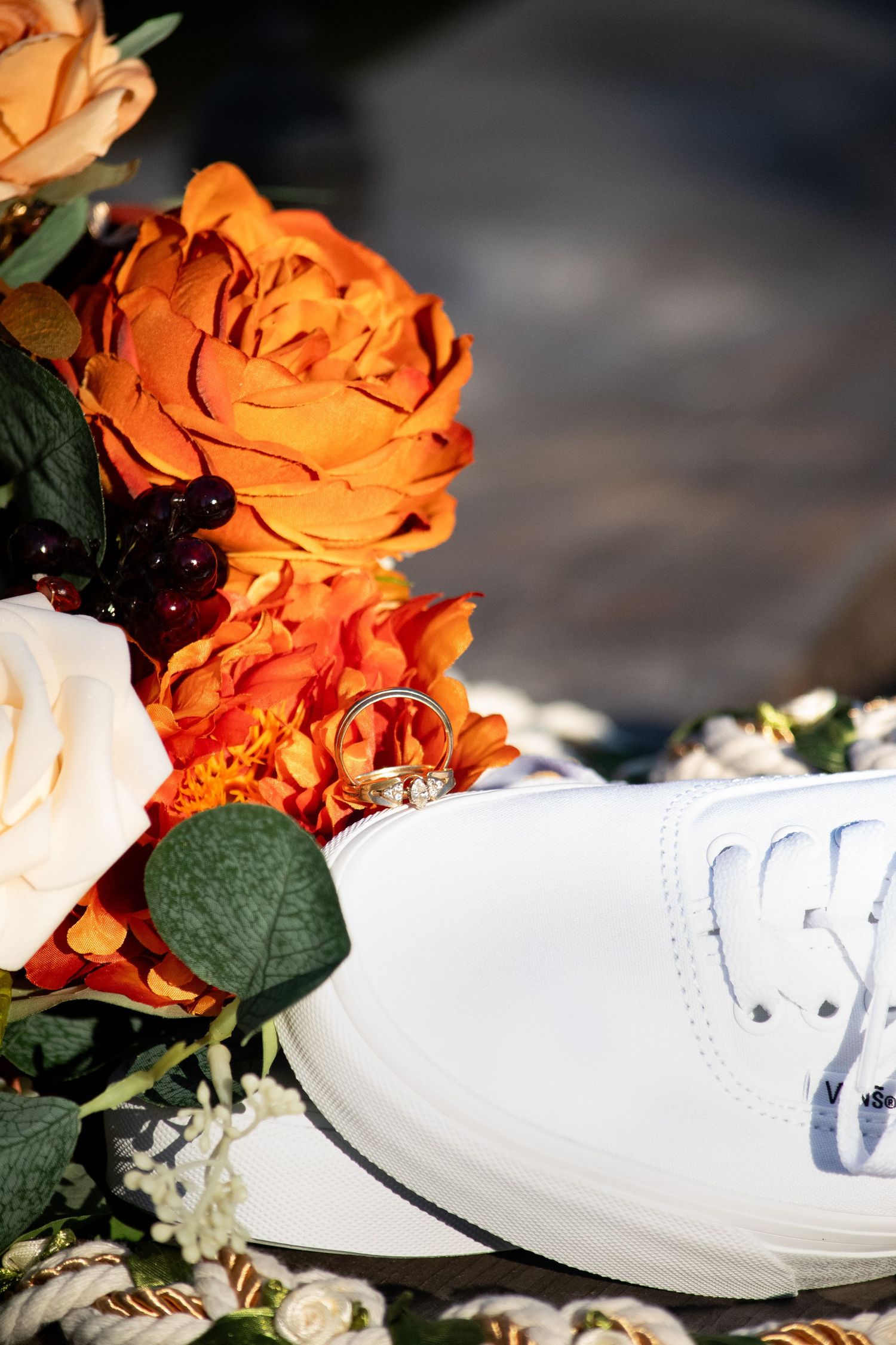 White sneaker with wedding rings resting on colorful orange and white floral bouquet arrangement.