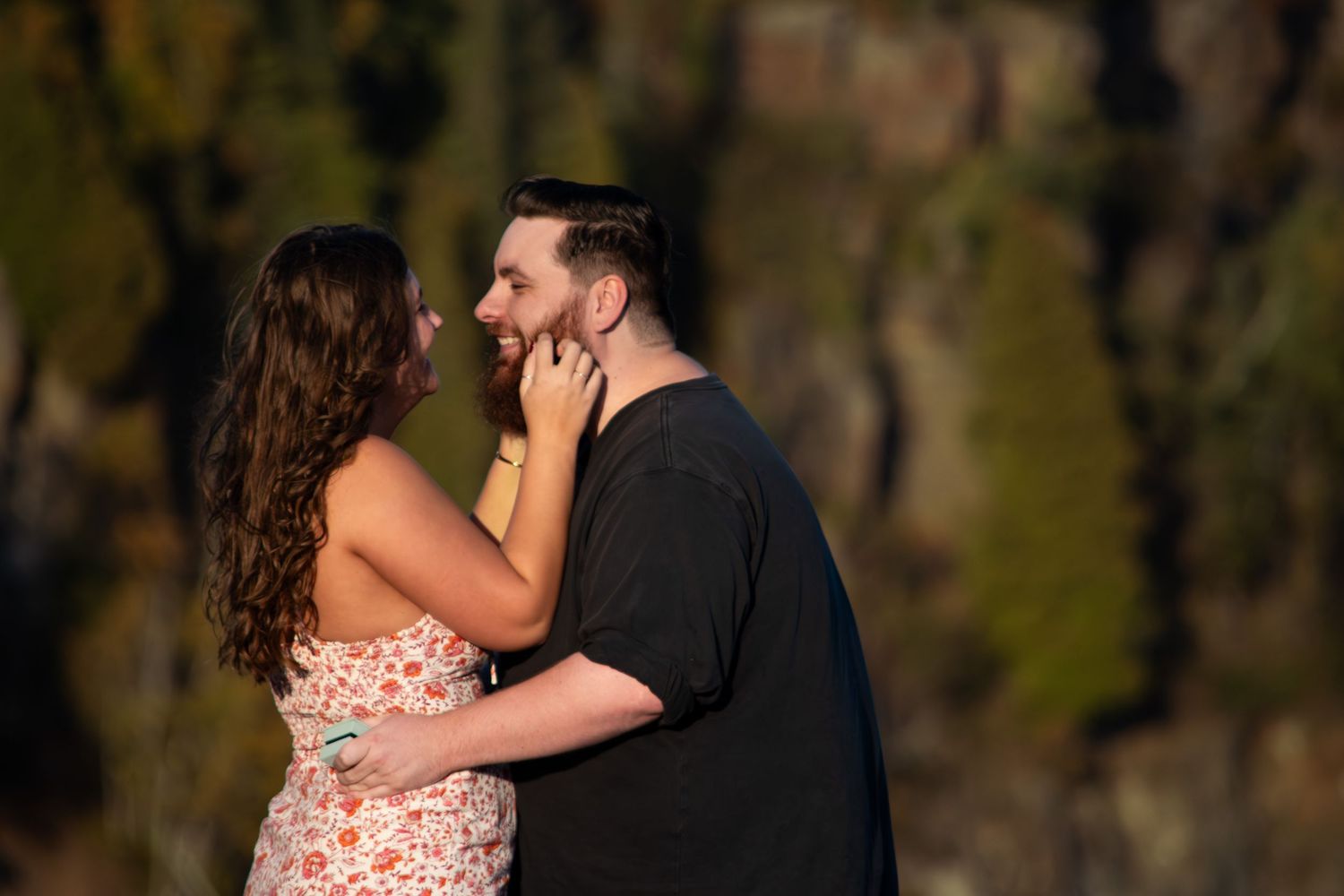 Newly engaged couple gazes at each other tenderly with autumn foliage behind them.