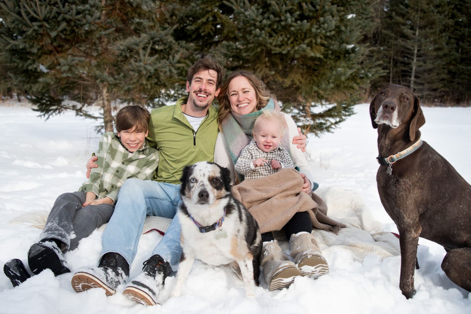 Happy family with two boys and two dogs sitting together in snowy winter landscape.
