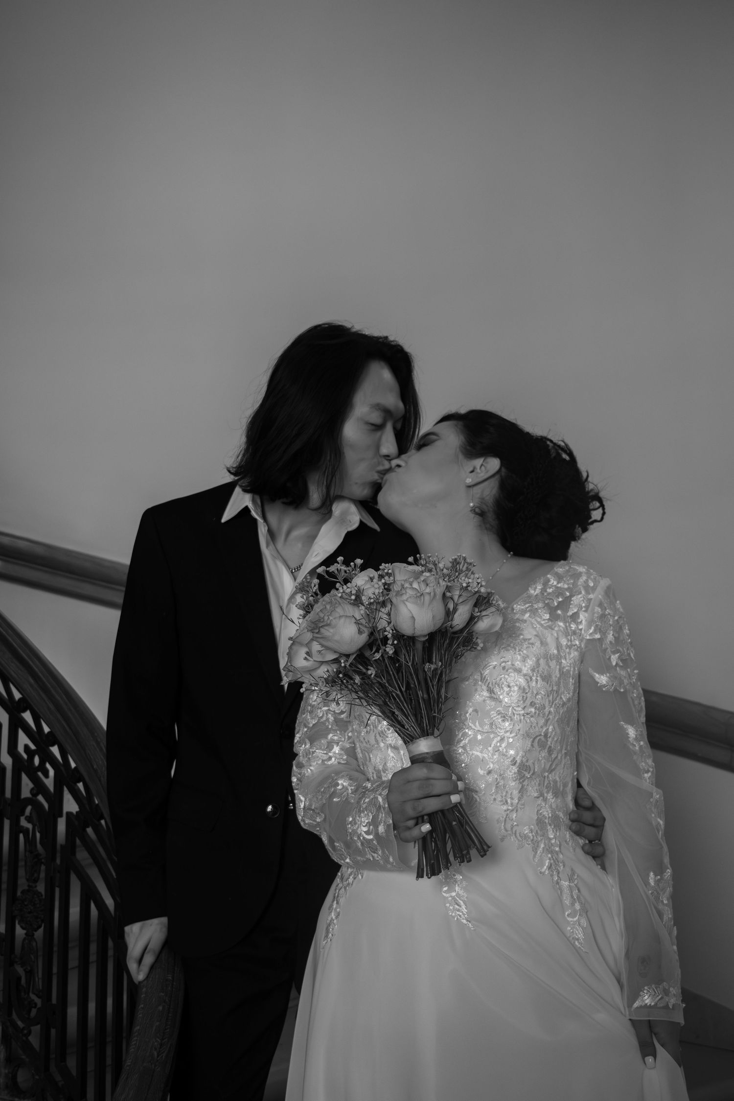 Black and white photo of bride and groom kissing on staircase with bouquet.