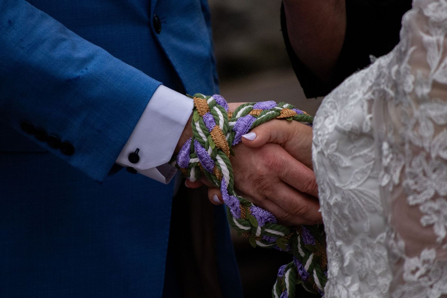 Couple holding hands bound together with colorful braided cord during a handfasting wedding ceremony.