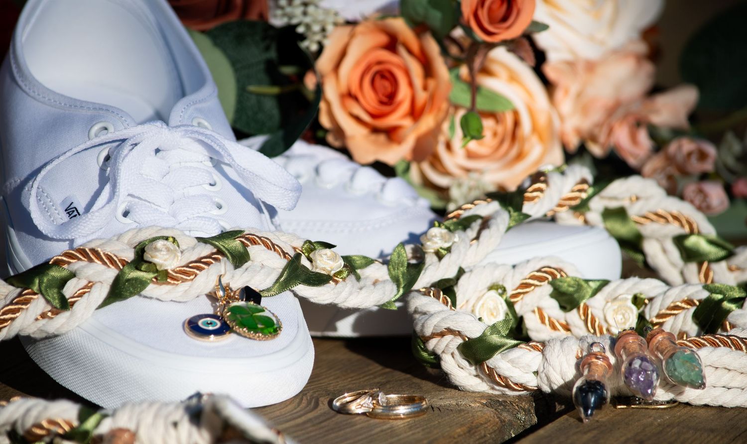 White sneakers with floral rope laces beside wedding rings and peach rose bouquet on wood surface.