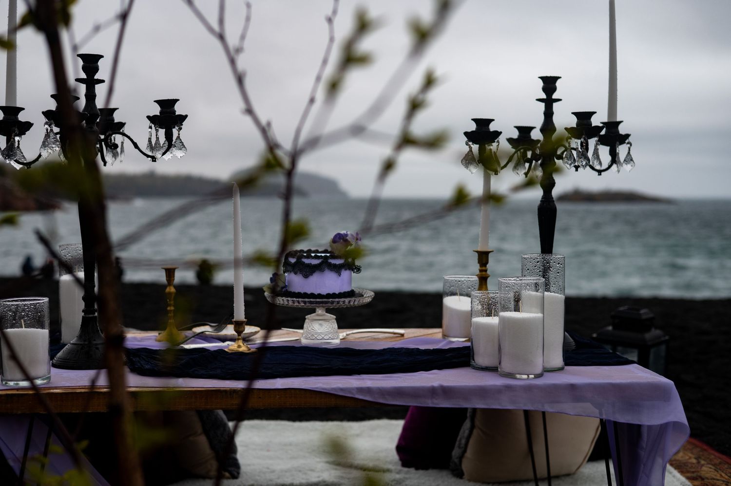 Elegant outdoor wedding table with purple cloth, candelabras, and white candles by the ocean on a cloudy day.