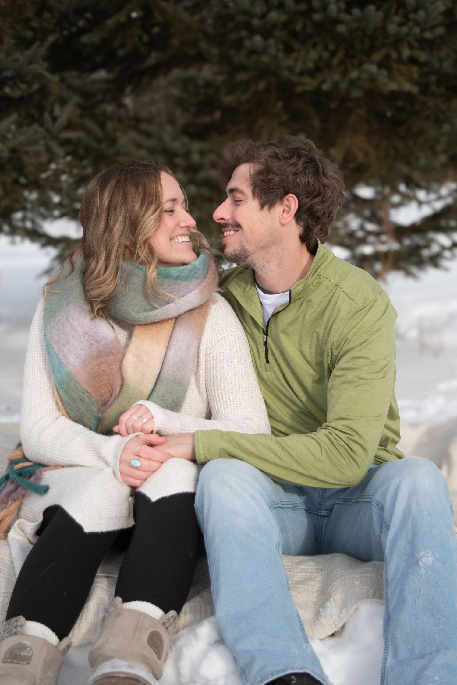 Loving couple holding hands and smiling at each other while sitting in snowy winter setting.