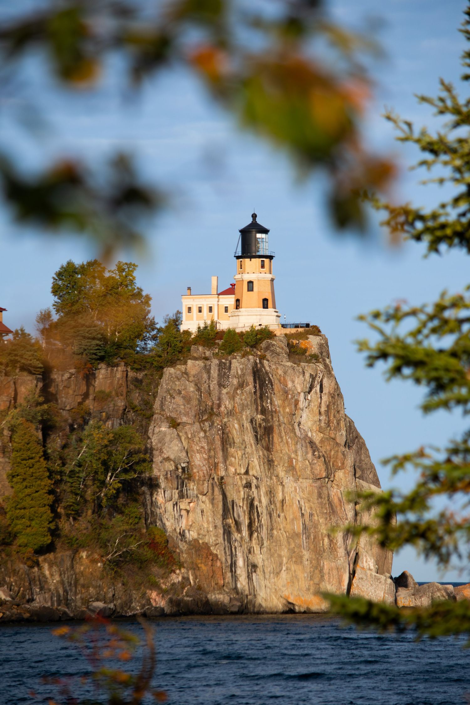 Split Rock Lighthouse perched on dramatic cliff above Lake Superior framed by autumn leaves.