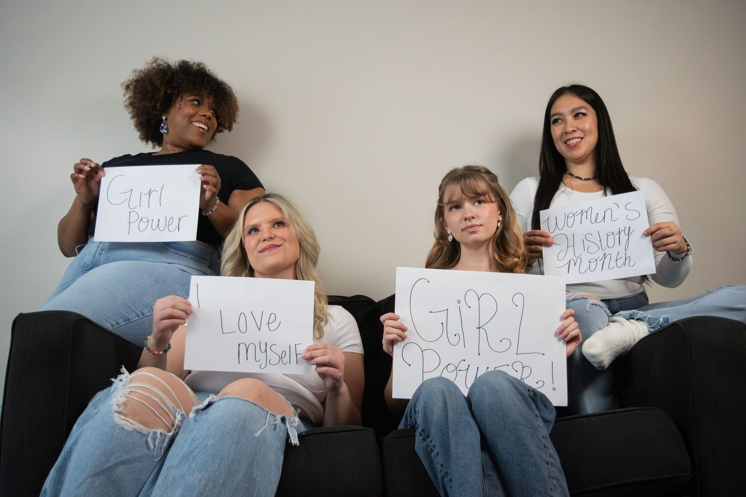 Four diverse women on a couch holding signs reading Girl Power, Love Myself, and Female Empowerment.