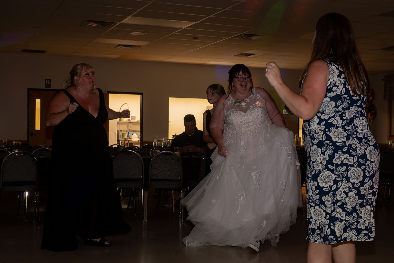 Bride in white wedding gown dancing with guests at indoor wedding reception celebration.