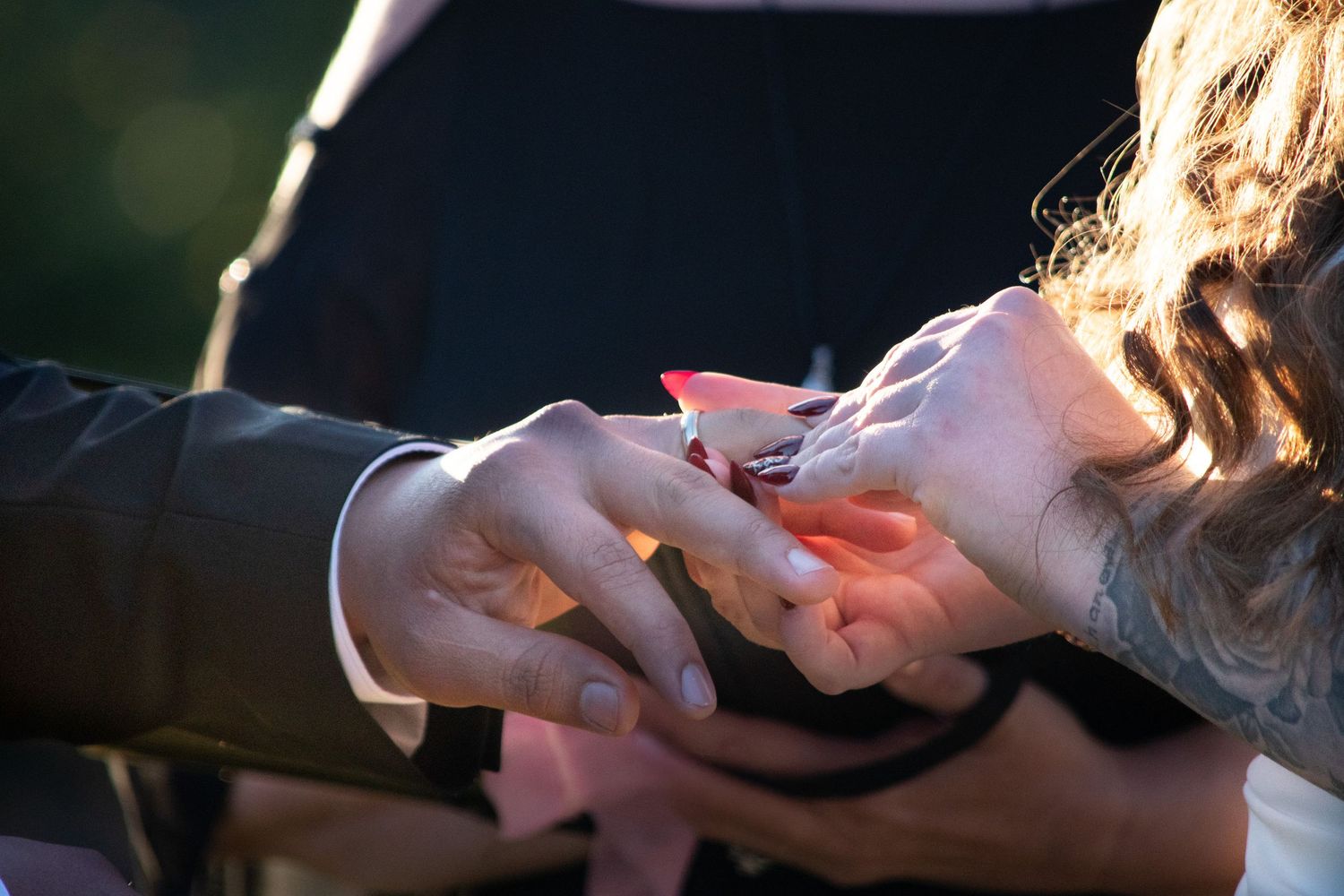 Close-up of groom placing wedding ring on bride's finger during outdoor ceremony.