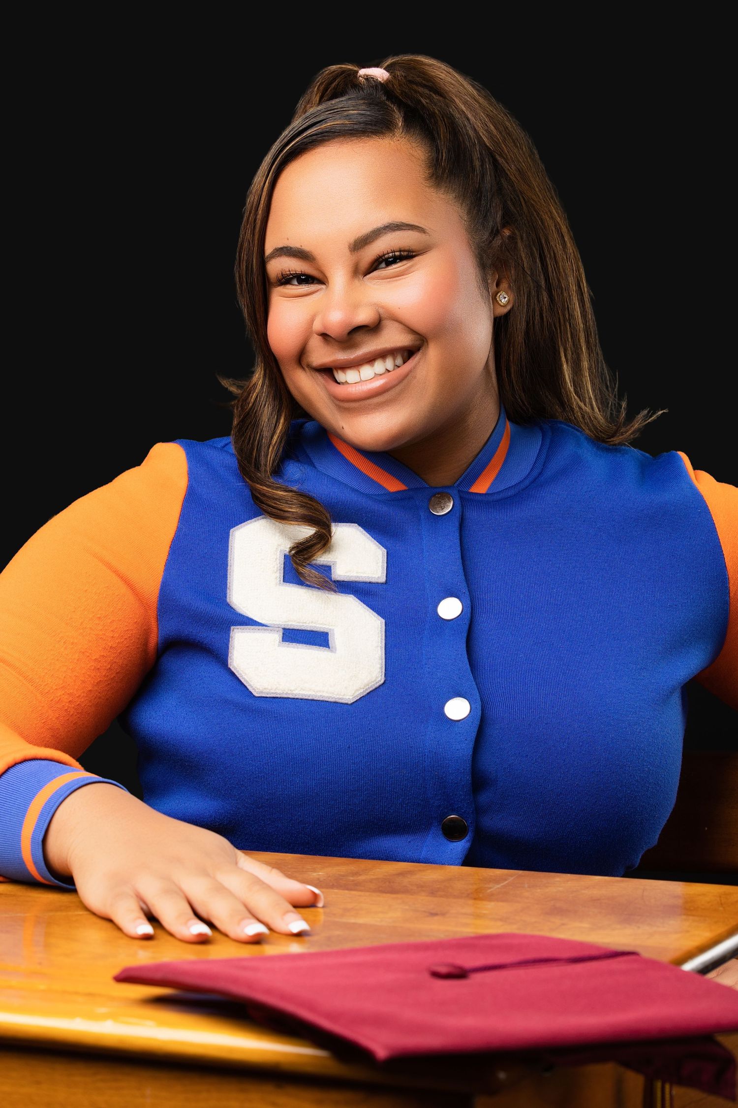 Person in blue and orange varsity jacket sits at desk with academic materials.