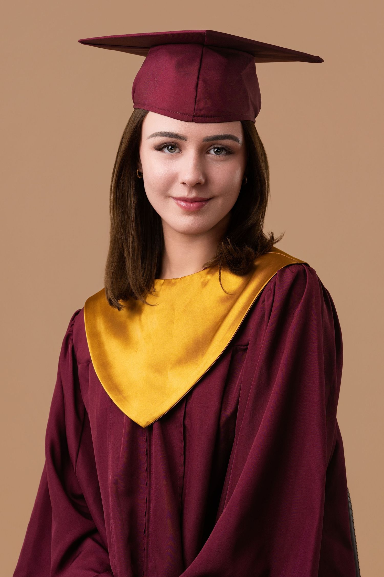 Graduate in maroon and gold academic regalia poses against neutral background.